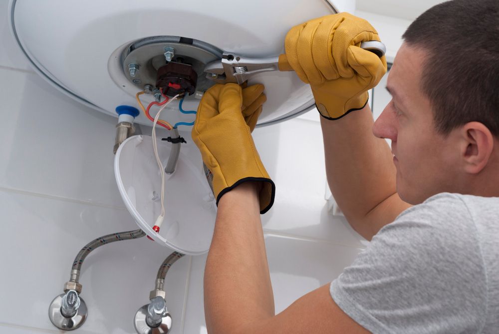 A Man Is Fixing A Water Heater With A Wrench — In Electrics In Innisfail, QLD