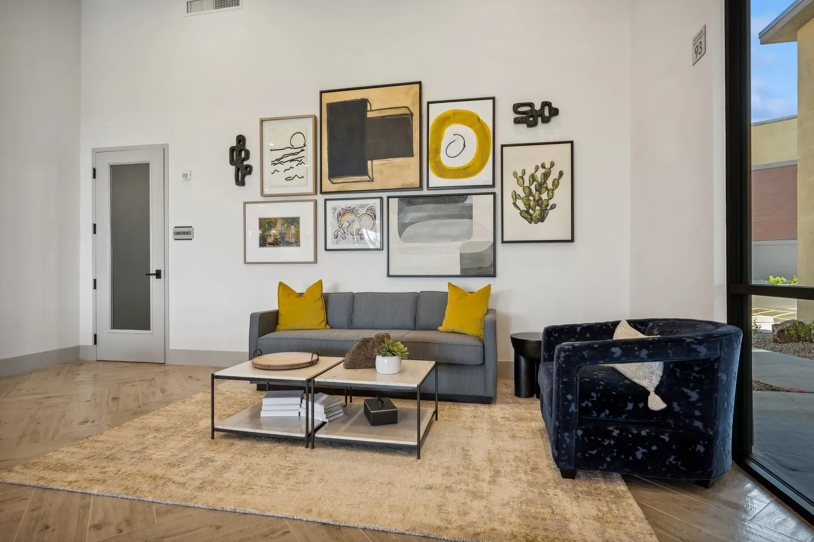 Modern living room area with gray sofa, blue armchair, coffee tables, and abstract art on the wall at Longbow Luxury Apartments Mesa, AZ.
