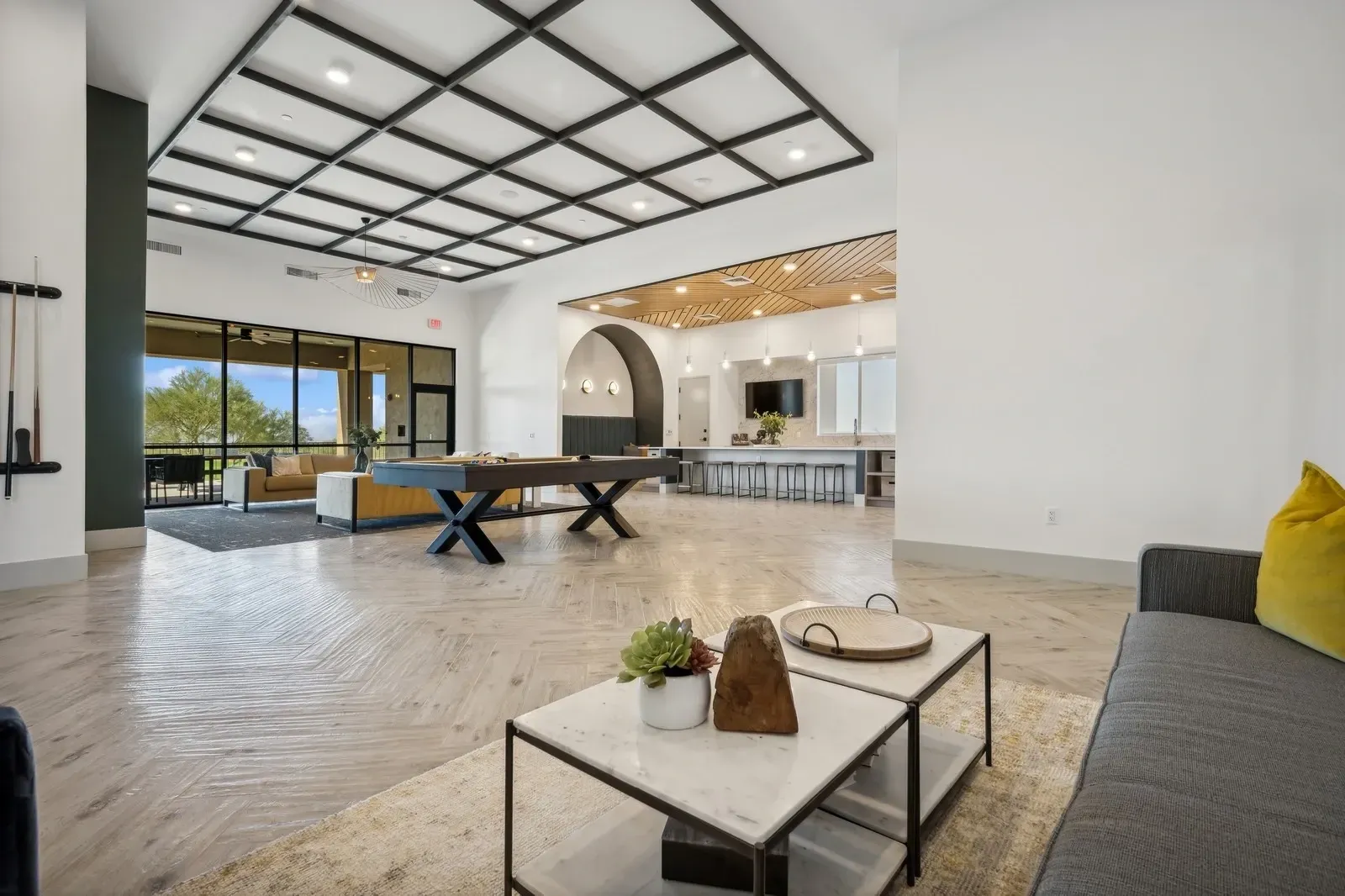 Modern lounge area with a pool table, bar seating, and comfortable seating with large windows at Longbow Luxury Apartments Mesa, AZ.