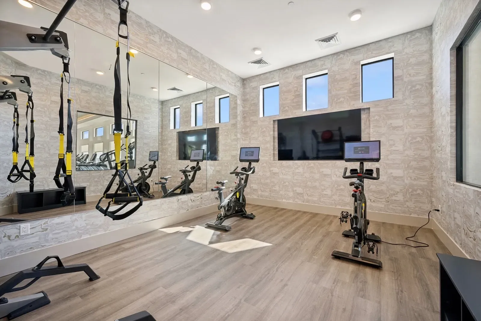 Fitness center with cardio equipment, TRX suspension trainers, and a large mirror at Longbow Luxury Apartments Mesa, AZ.