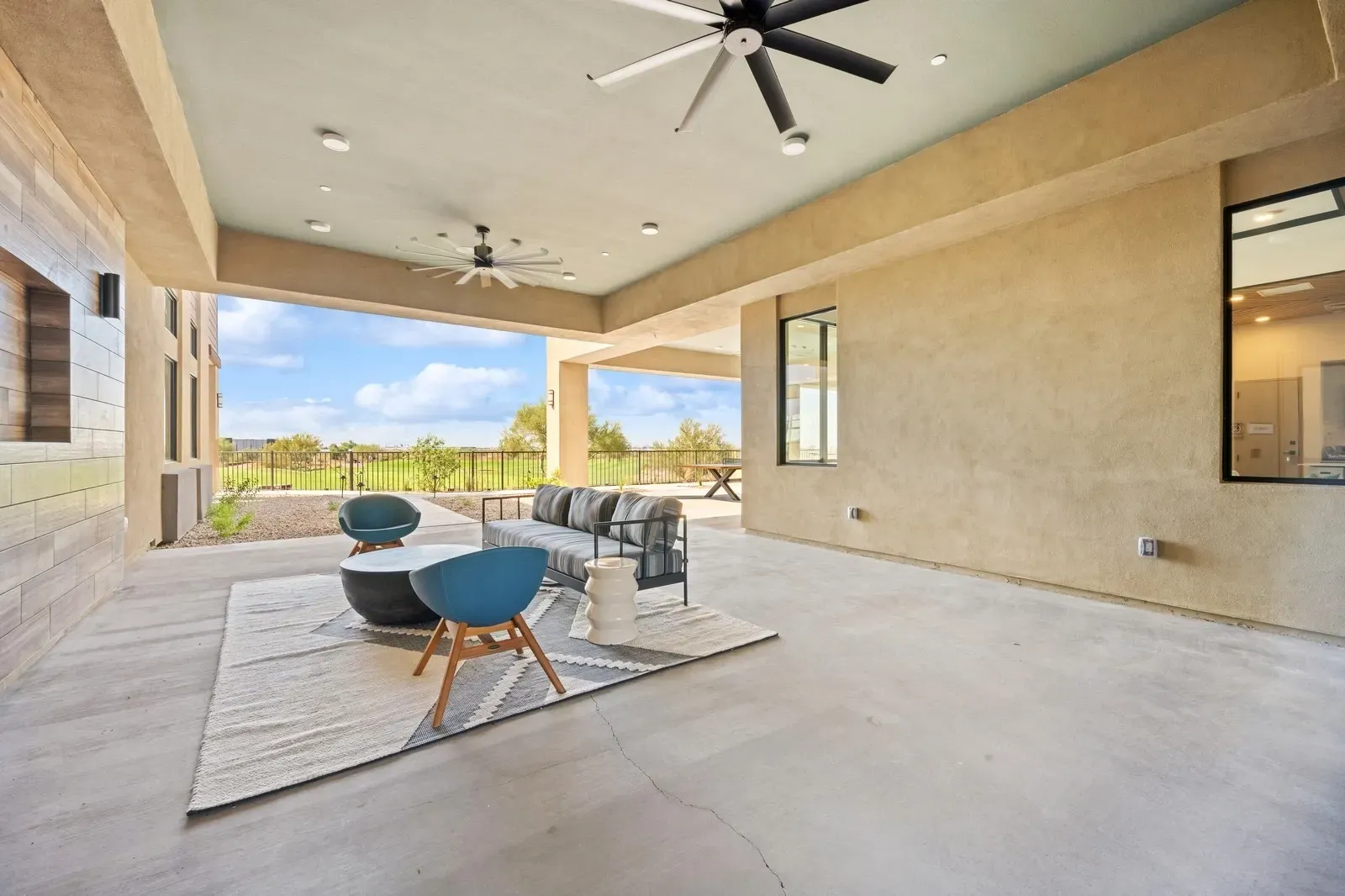 Covered outdoor patio with modern seating and ceiling fans, overlooking a green landscape at Longbow Luxury Apartments Mesa, AZ.