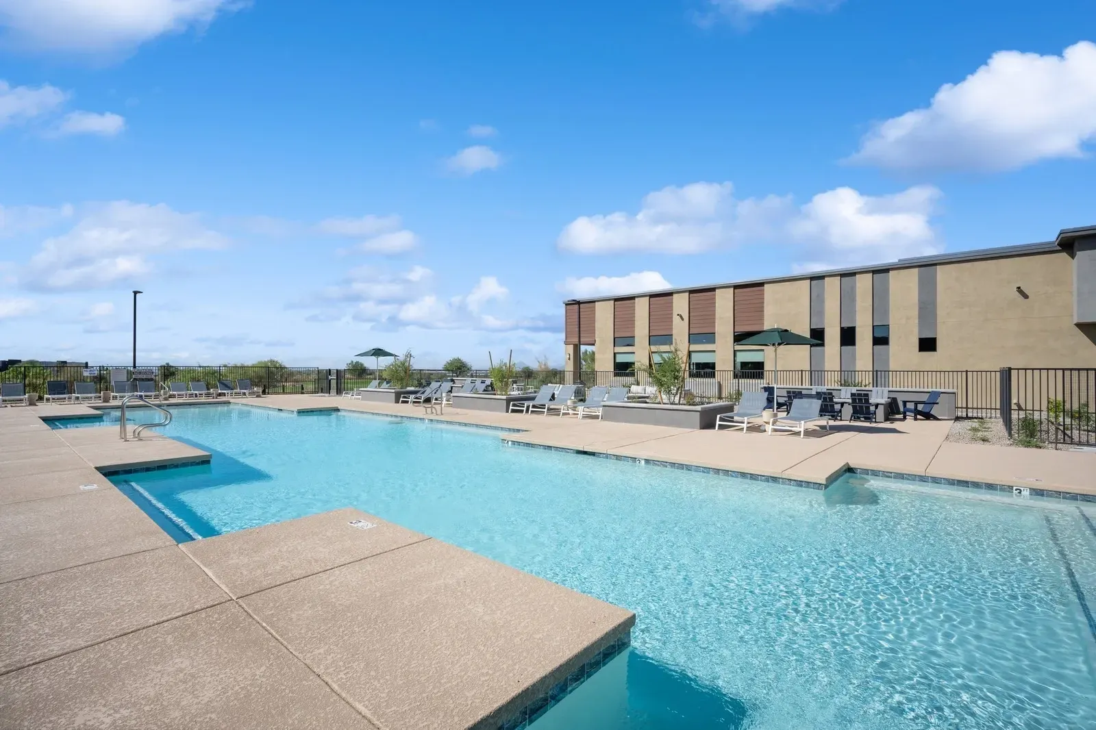 Outdoor swimming pool with lounge chairs and umbrellas, next to a modern building.