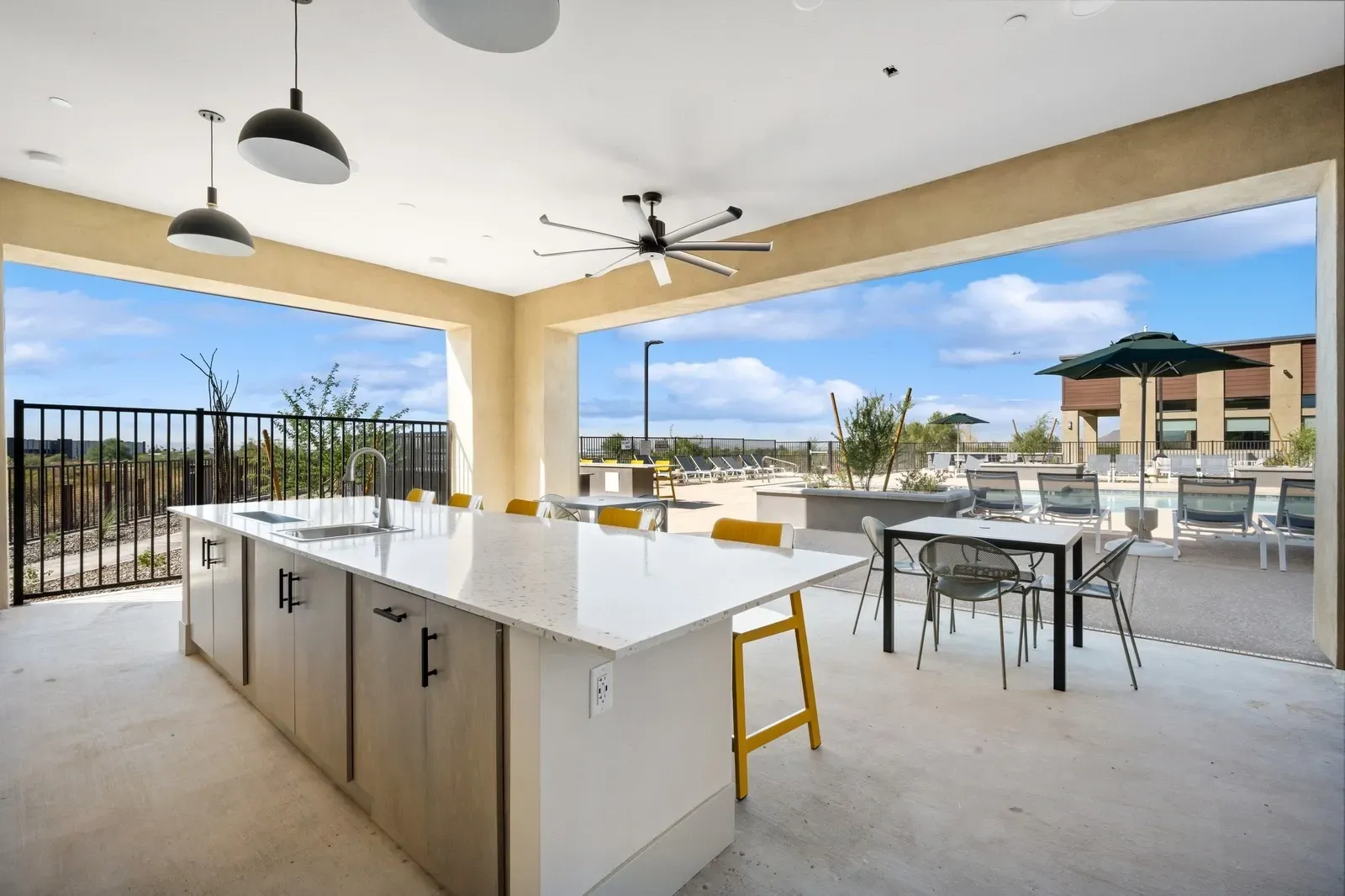 Outdoor kitchen island with sink and stools, overlooking a swimming pool and lounge chairs.