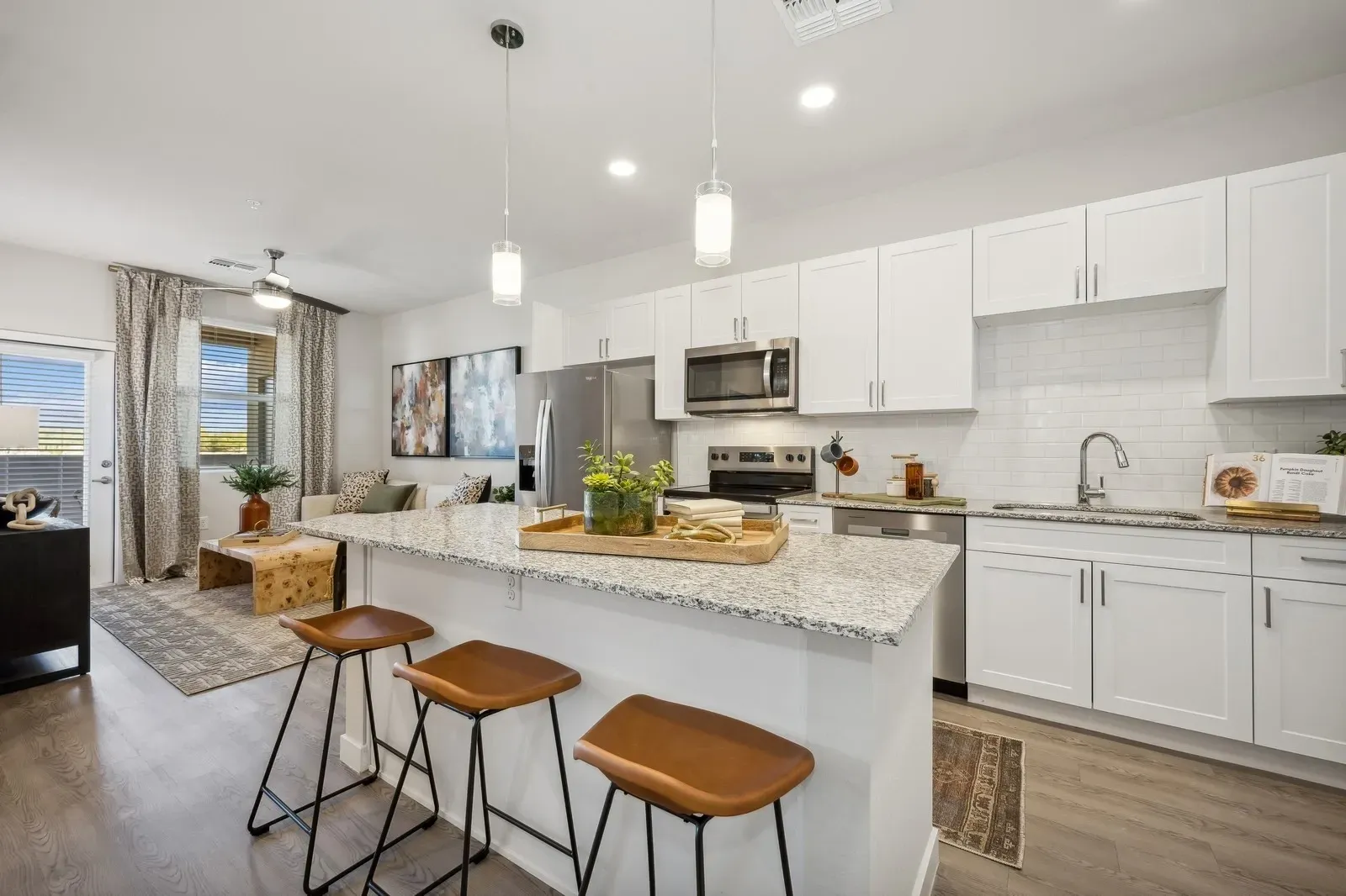 Modern kitchen with granite countertops and stainless steel appliances, open to a living area with a sofa at Longbow Luxury Apartments Mesa, AZ.