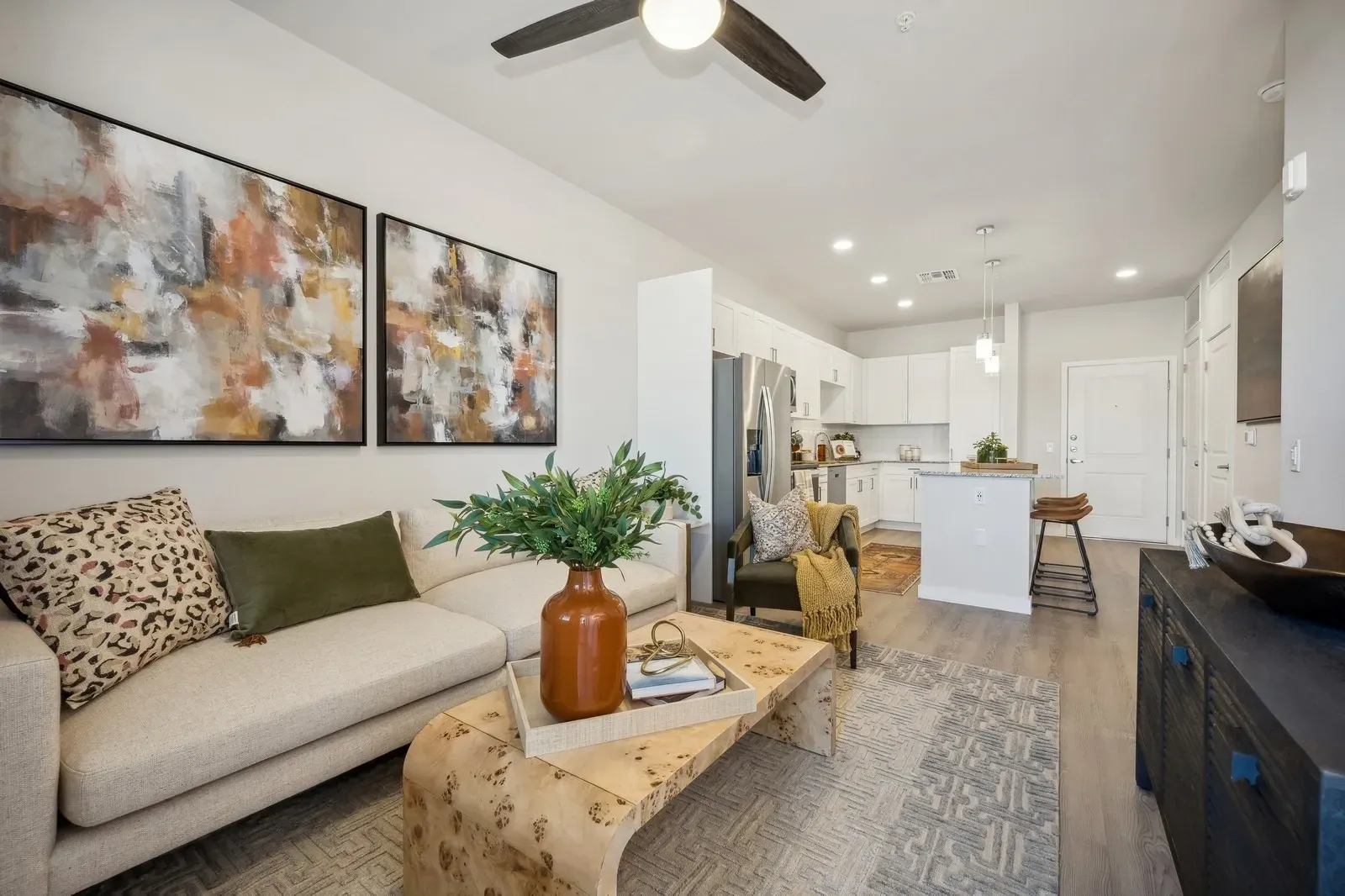Bright and airy living room with a modern aesthetic, featuring abstract art, a comfortable sofa, and an open-concept kitchen at Longbow Luxury Apartments Mesa, AZ.