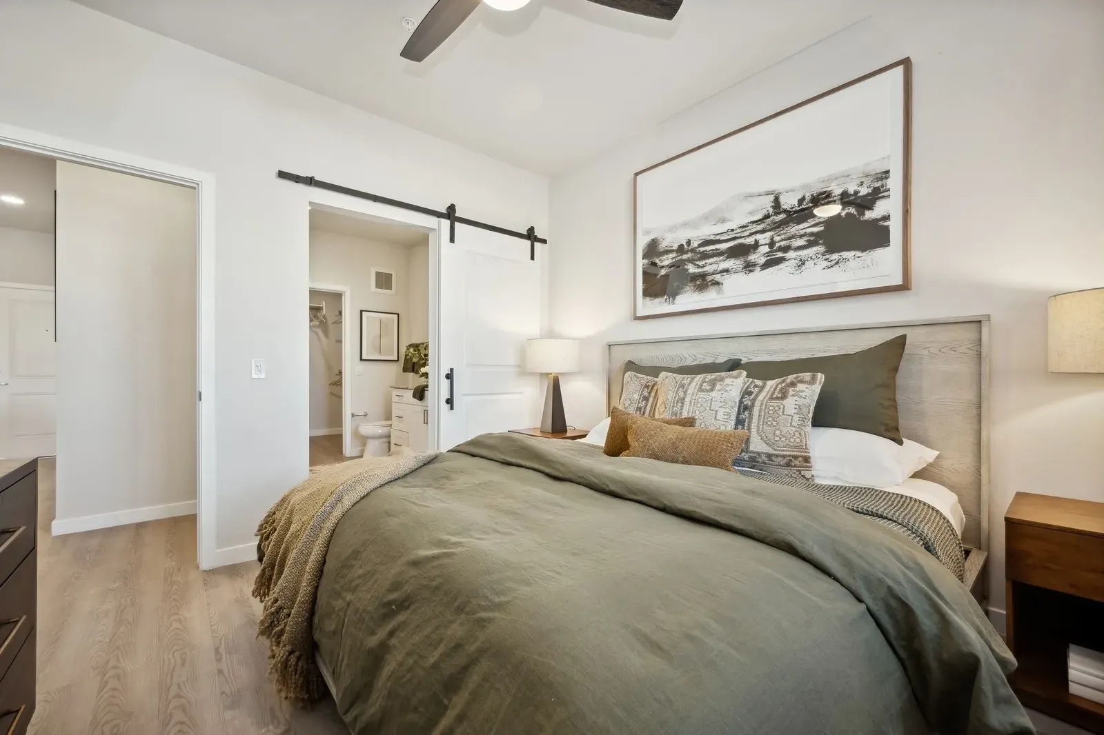 Primary bedroom with a bed, barn door, and en-suite bathroom at Longbow Luxury Apartments Mesa, AZ.