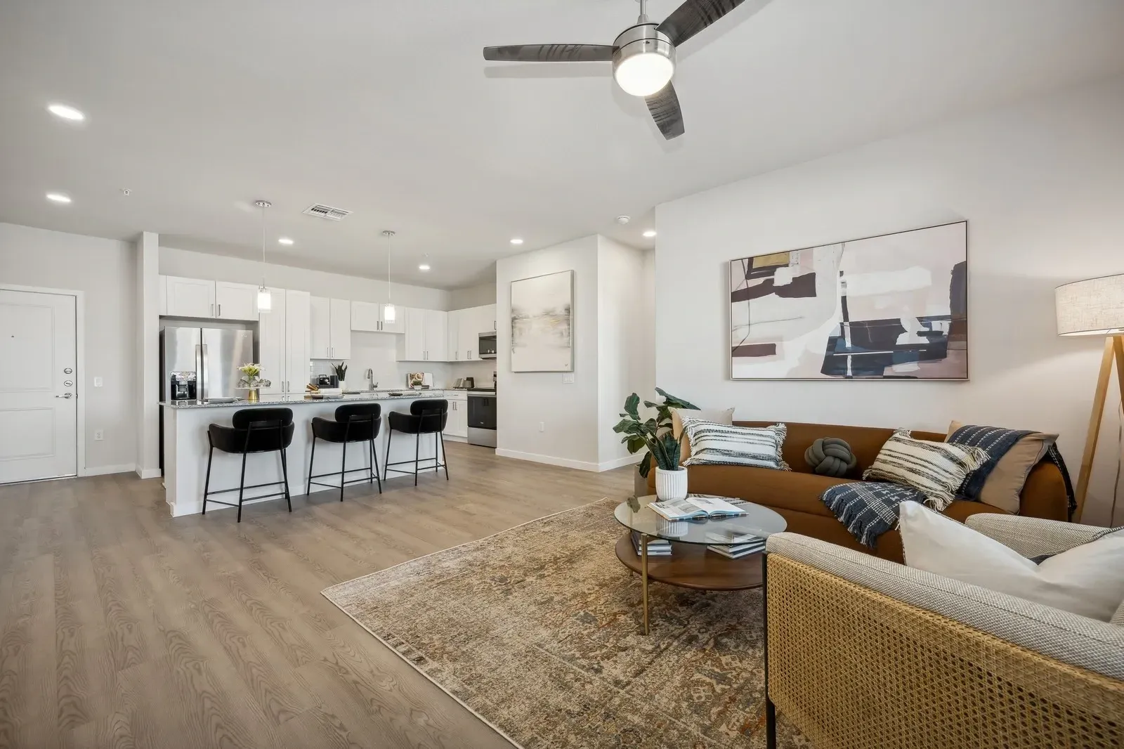 Open-concept living room and kitchen with modern furnishings, including a sofa, coffee table, and kitchen island with bar stools at Longbow Luxury apartments in Mesa, AZ.
