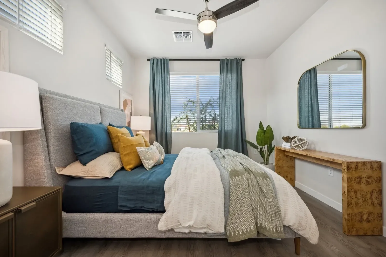 Modern bedroom with a large bed, ceiling fan, and a mirror  at Longbow Luxury Apartments Mesa, AZ.