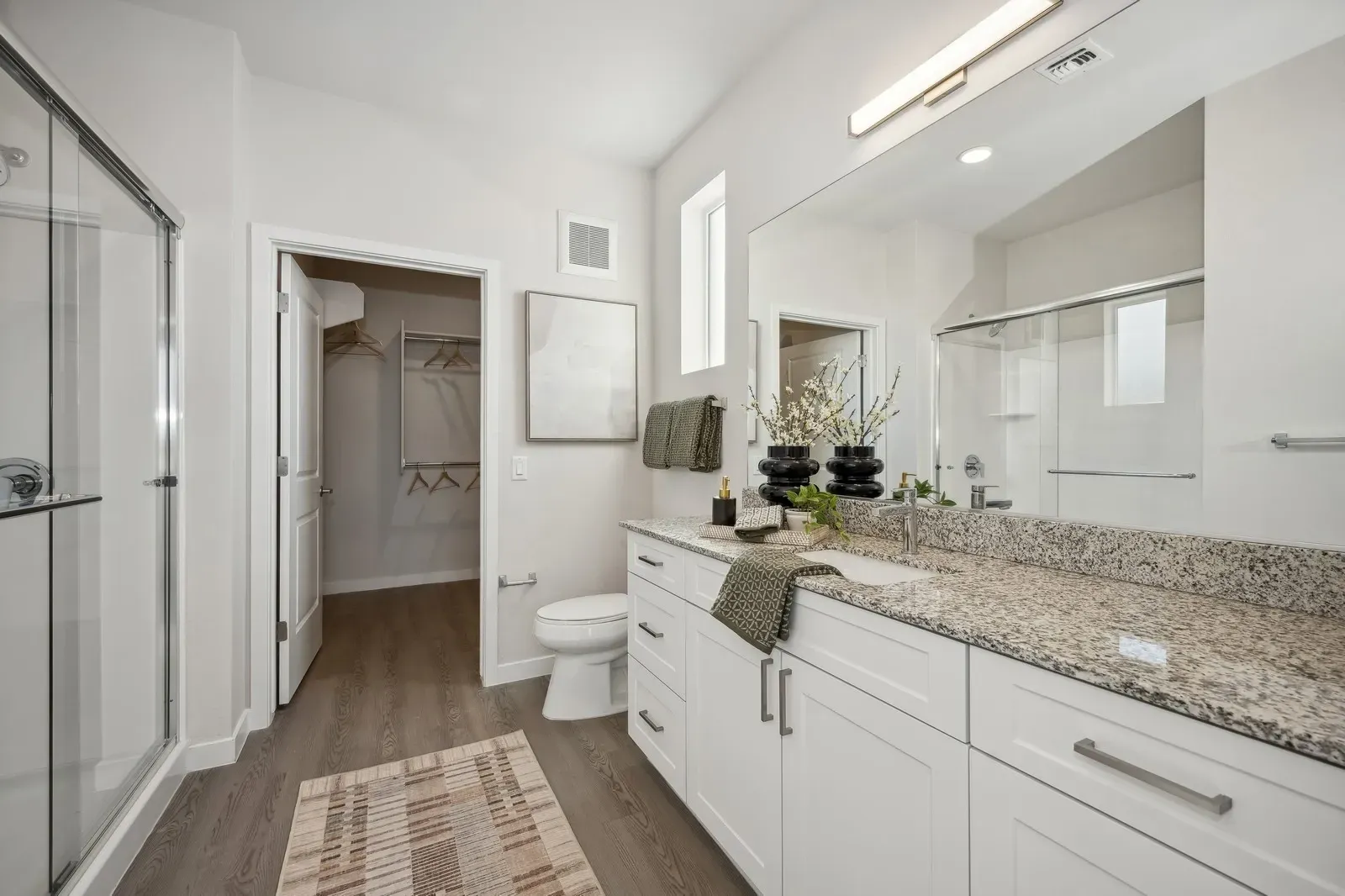 Modern bathroom with double vanity, granite countertops, glass-enclosed shower, and walk-in closet.