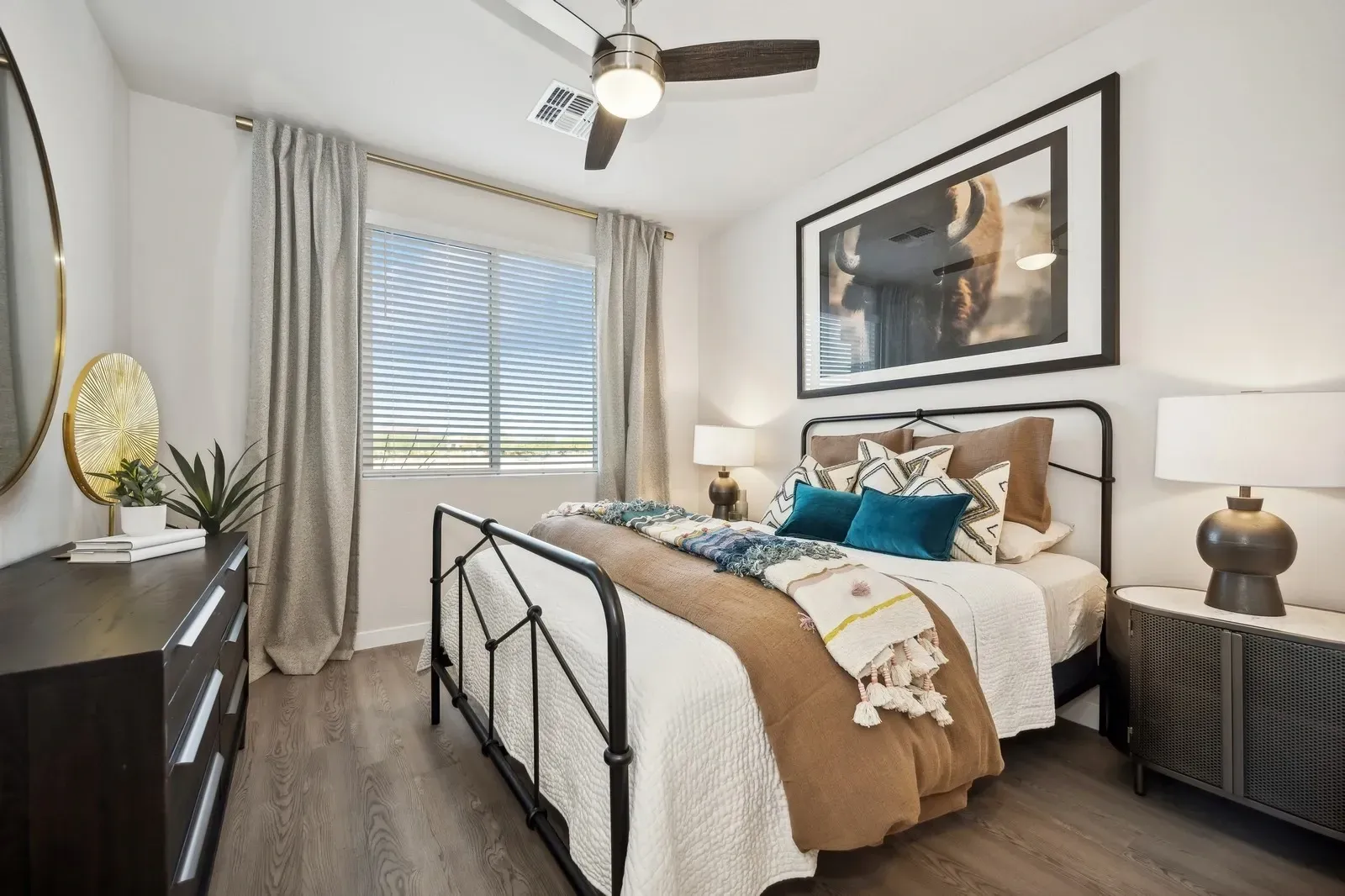 Bedroom with a large framed picture of a bison, a ceiling fan, and a dresser at Longbow Luxury Apartments Mesa, AZ.