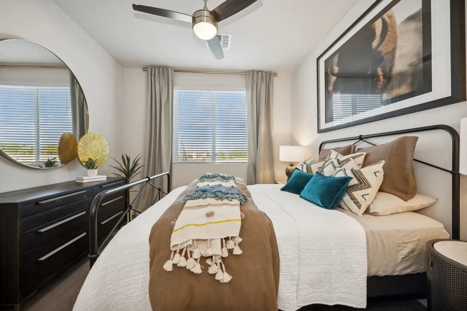 Stylish bedroom with a large framed artwork above the bed and a round mirror on the dresser at Longbow Luxury Apartments Mesa, AZ.