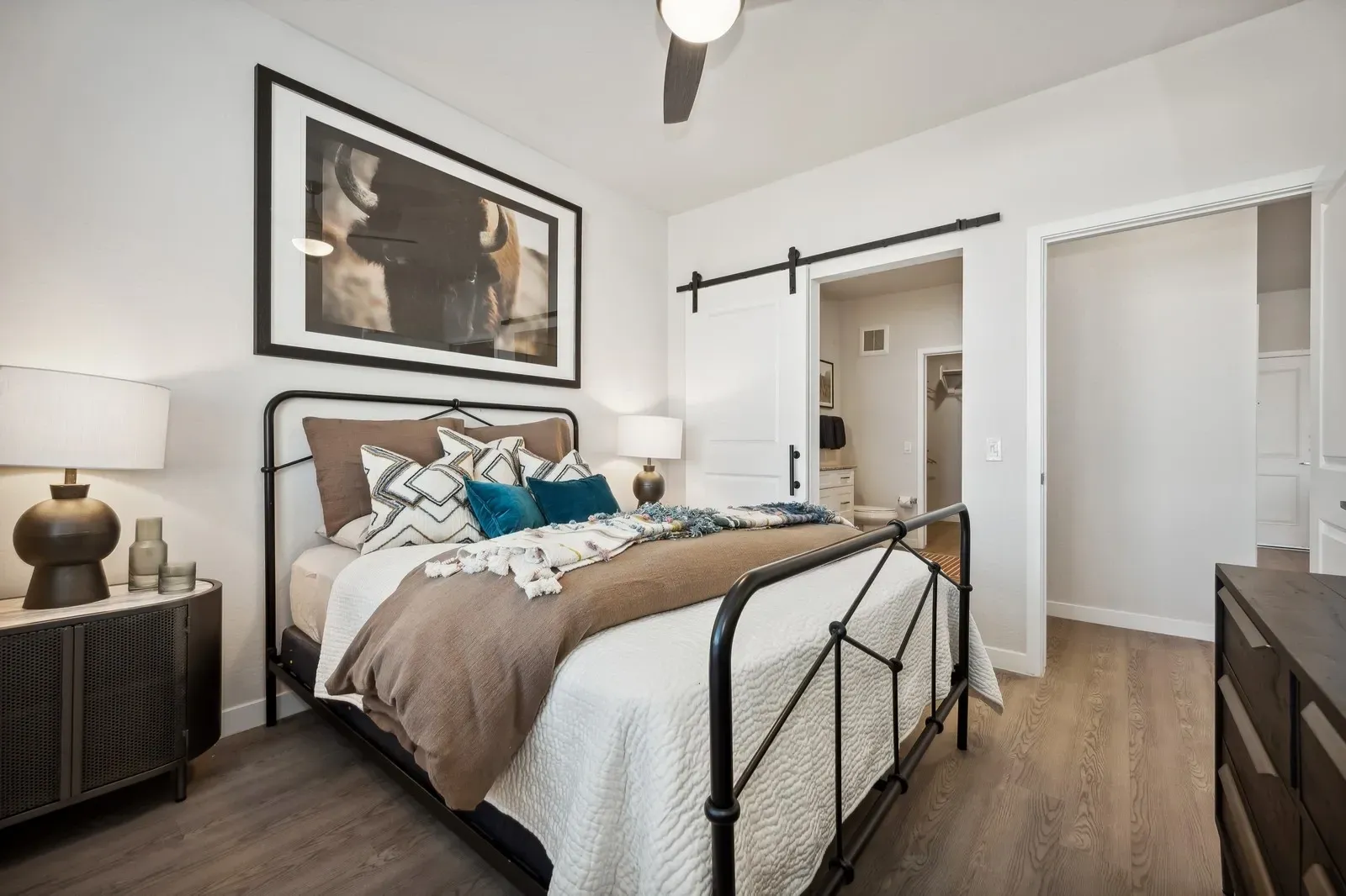 Stylish bedroom with a large framed artwork, a sliding barn door, and a comfortable bed at Longbow Luxury Apartments Mesa, AZ.