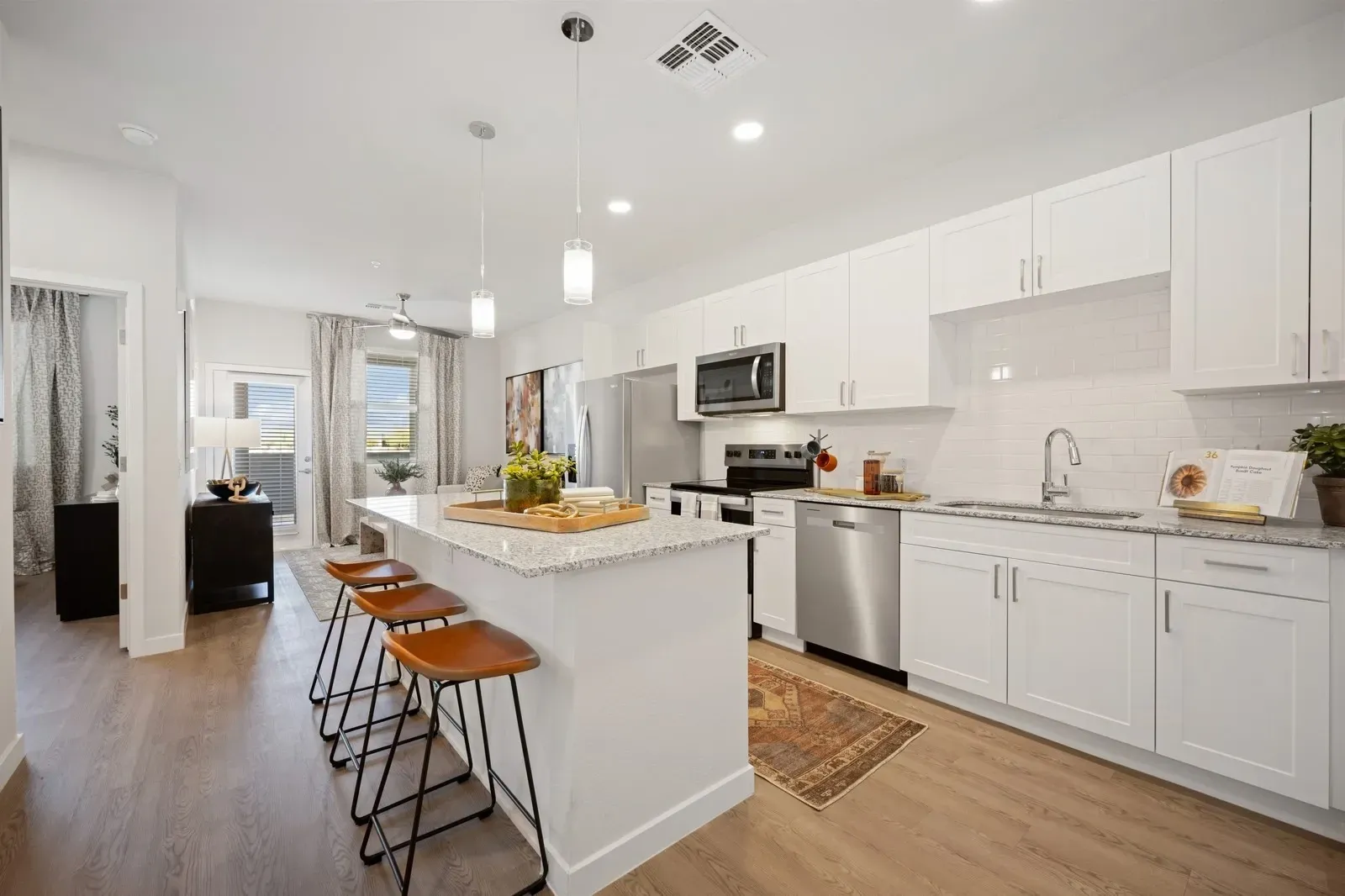 Modern kitchen with white cabinets, granite countertops, an island with bar stools, and stainless steel appliances  at Longbow Luxury Apartments Mesa, AZ.