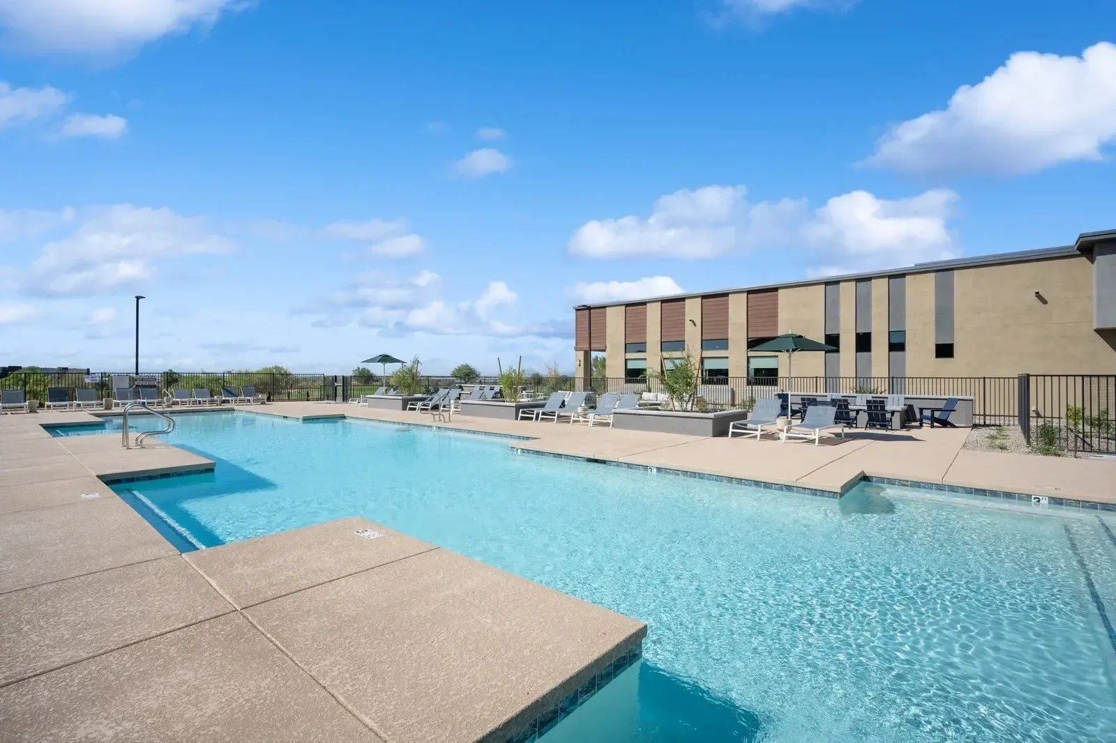 Outdoor swimming pool with lounge chairs and umbrellas at Longbow Luxury apartments in Mesa, AZ.
