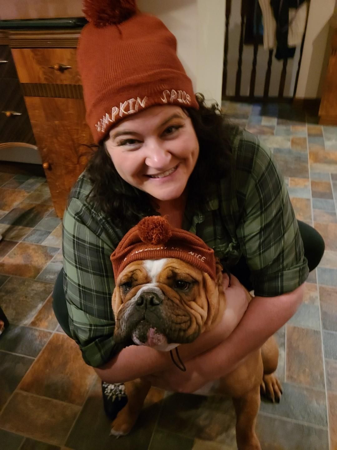 Woman hugging a bulldog indoors, both wearing matching orange knit hats
