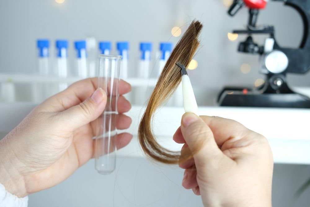 Hands holding hair strand with tweezers next to an empty test tube and a microscope in a lab setting — DAB Services in Cannonvale, QLD