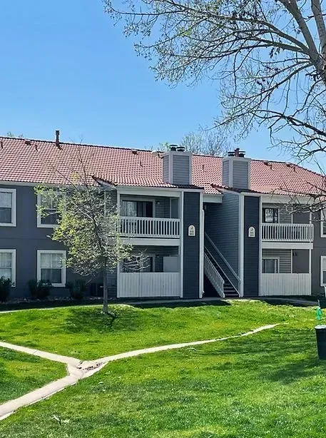 Apartment building with gray siding, white balconies, and red tile roof, on a grassy lawn under a blue sky.