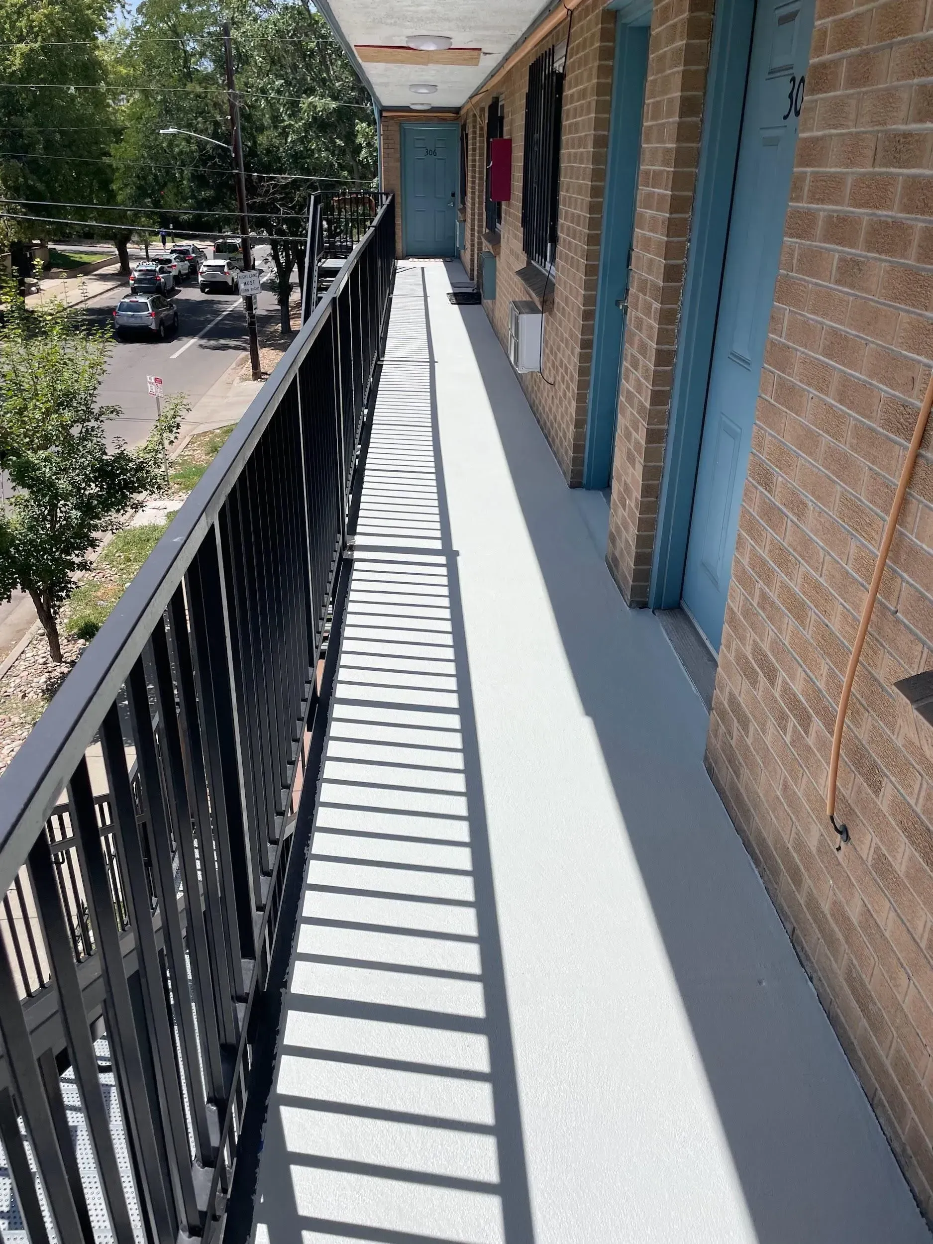 Exterior apartment hallway with black railing, gray flooring, and brick walls.