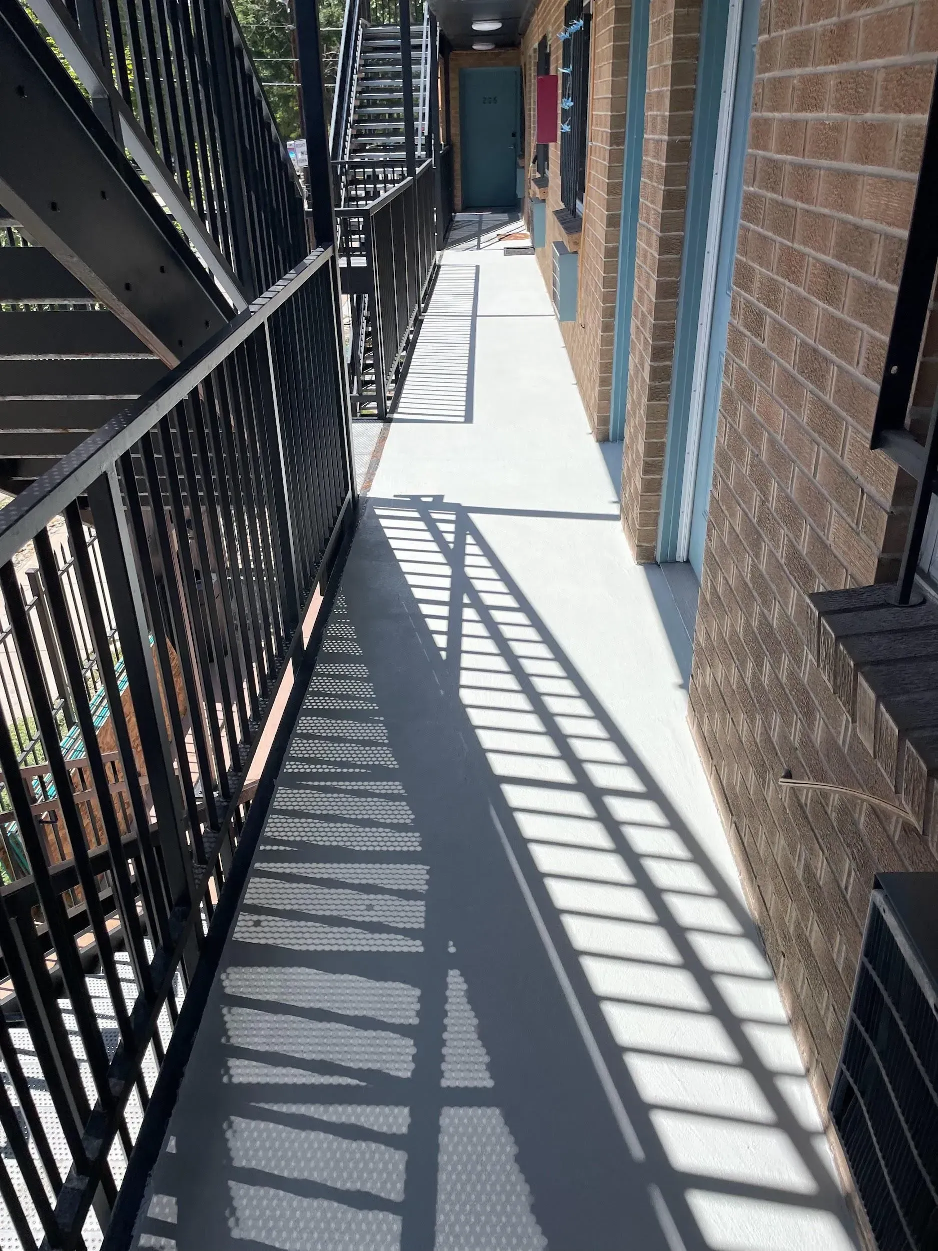 Exterior apartment walkway with metal railings and long shadow.