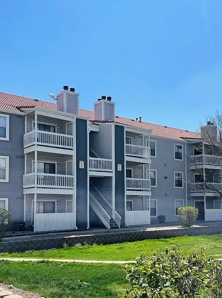 Apartment building with blue siding, white balconies, and red tile roof against a blue sky.