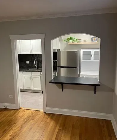 Interior view: doorway to kitchen, arched pass-through with fold-down counter, stainless steel refrigerator, wood floors.