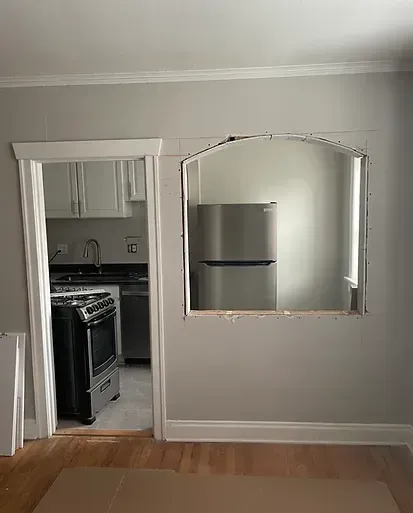 Interior view: A doorway and a rectangular opening in a gray wall reveal a kitchen with stainless steel appliances.