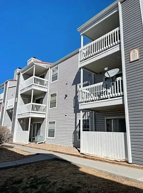 Multi-story apartment building with gray siding and white balconies under a clear, blue sky.