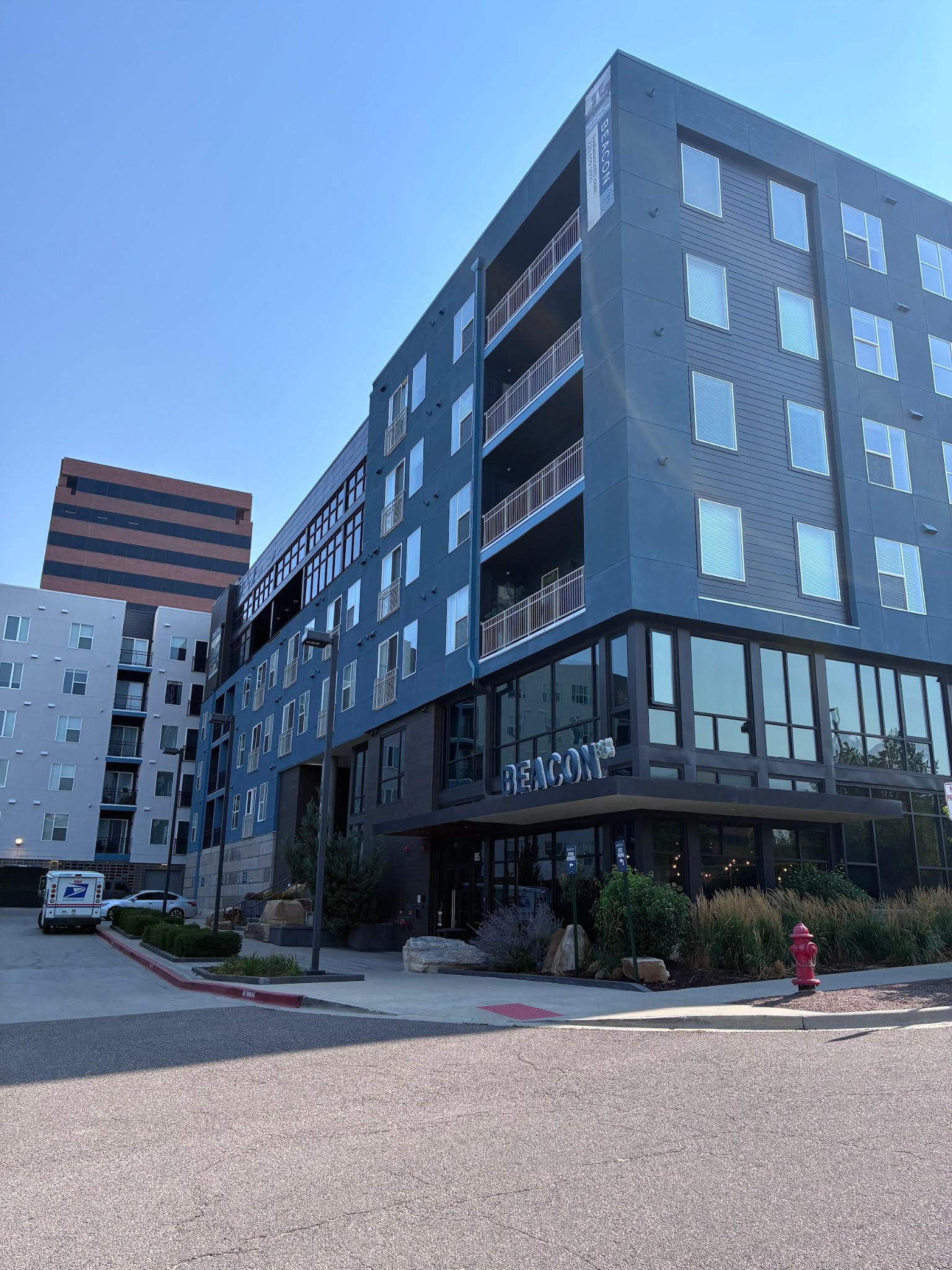 Modern apartment buildings with gray facades and balconies along a street under a blue sky.