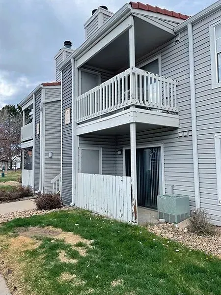 Two-story condo building with gray siding, white balcony, and red tile roof. Exterior view with grass and overcast sky.