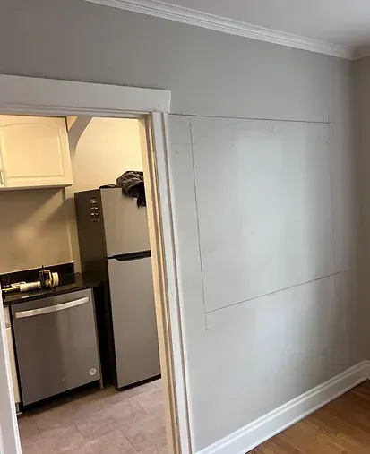 Interior view with a doorway leading to a kitchen; gray walls with a marked rectangle; white trim.
