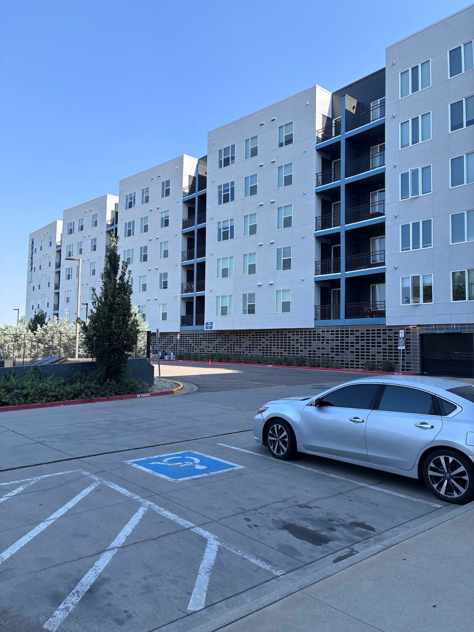 Apartment building parking lot with a silver car parked near a blue accessible space