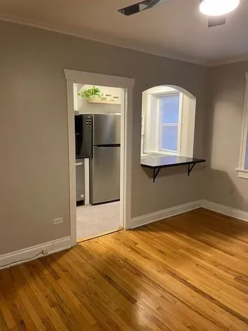 A doorway to a kitchen with a refrigerator, wooden floors, and a small counter near a window.