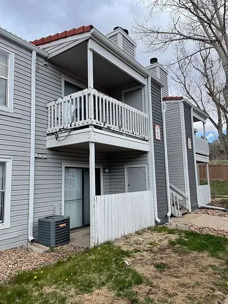 Two-story condo with a balcony, grey siding, and red tile roof. An AC unit and a white fence are visible.
