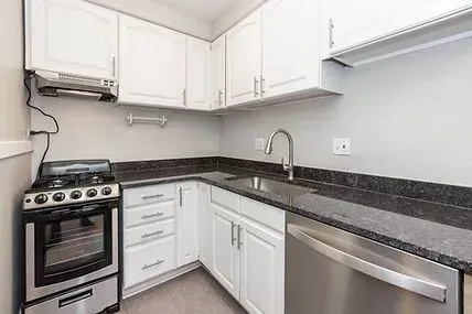 Small, white kitchen with stainless steel appliances, black countertops, and light gray walls.