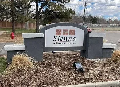 Sign for Sienna at Cherry Creek; gray, white, and brown, with solar panel at base.