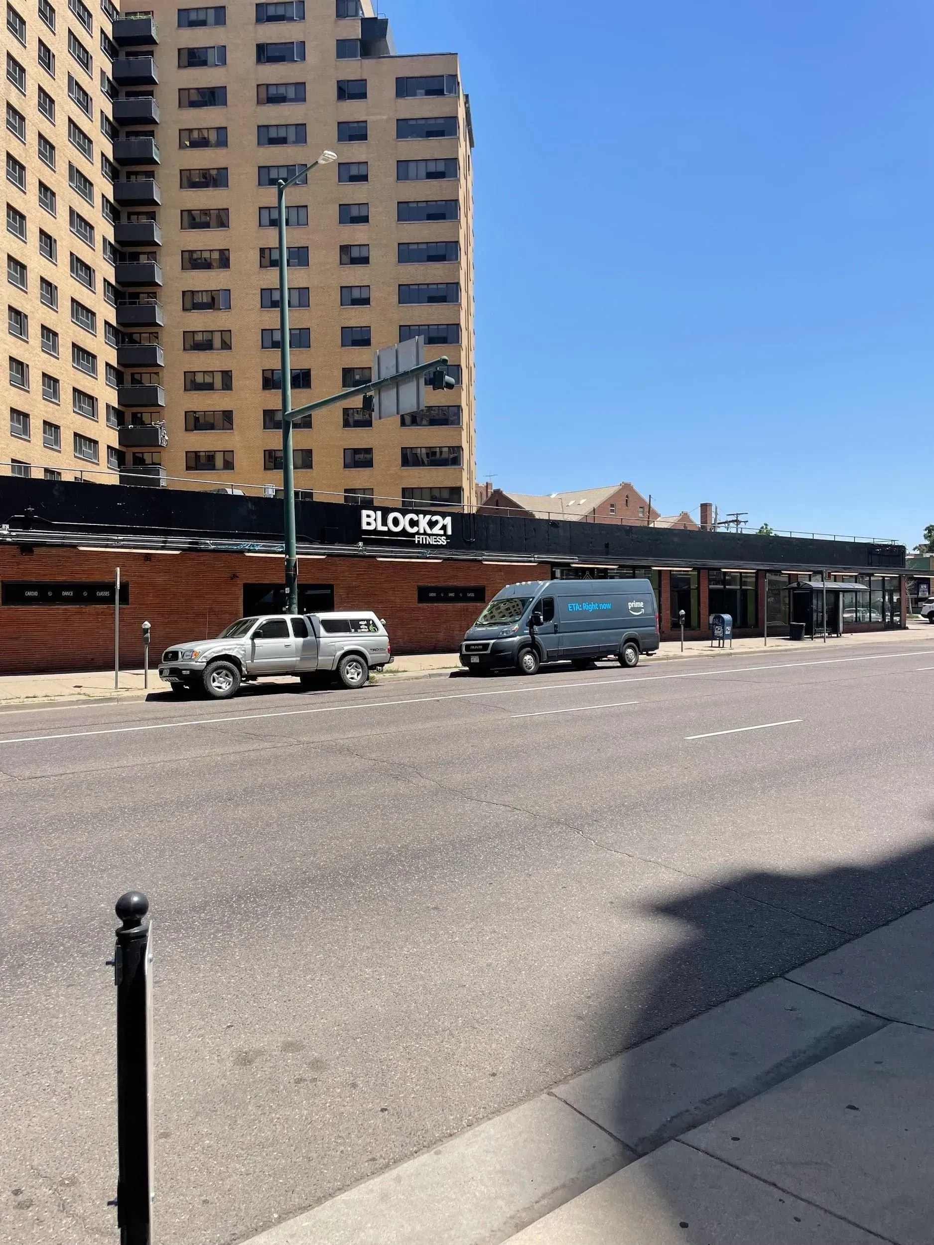 A street scene with a brick building and tall apartment building; a truck and van are parked.
