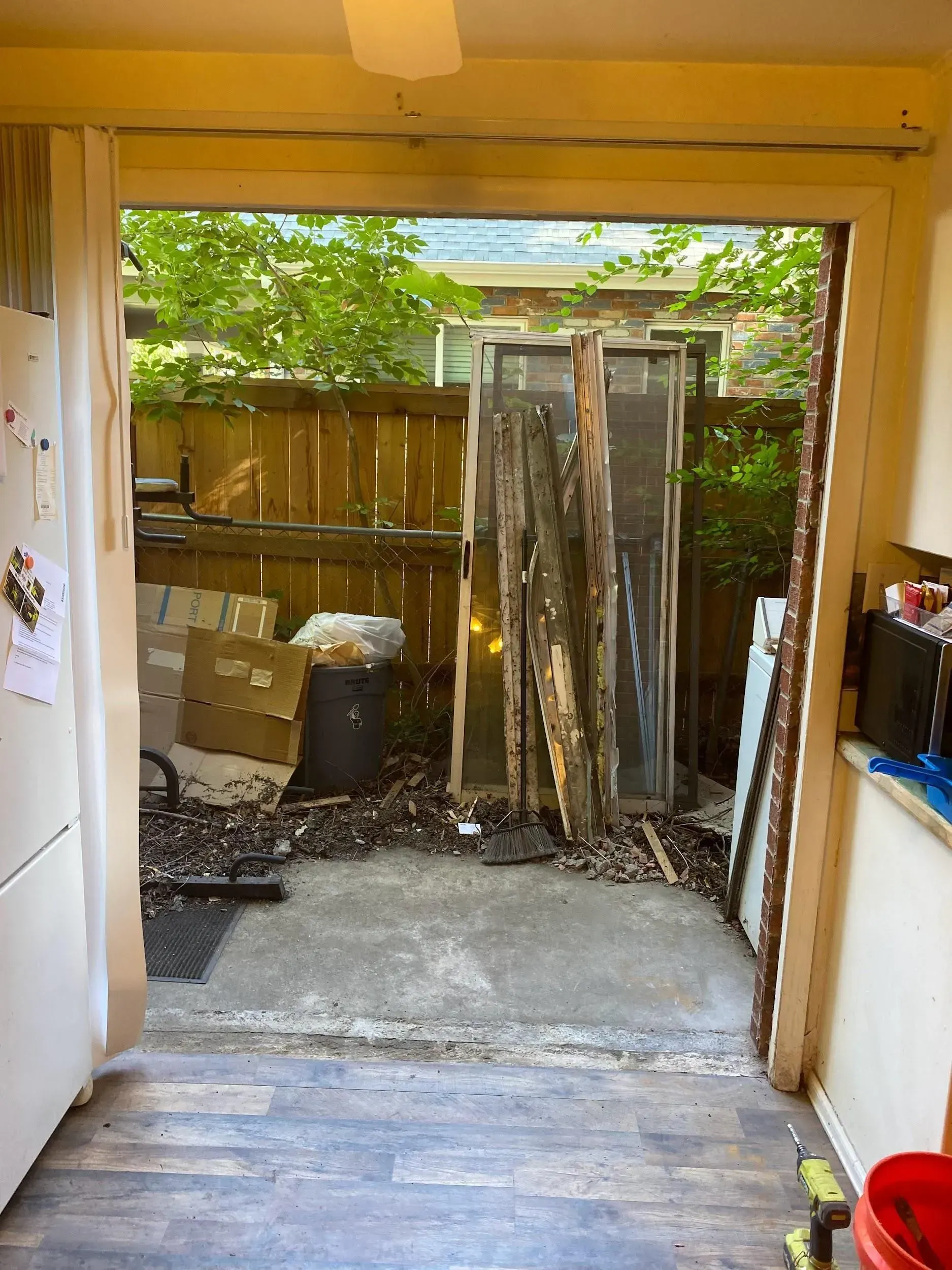 View from a room through an open doorway to a cluttered patio with old windows, a fence, and debris.