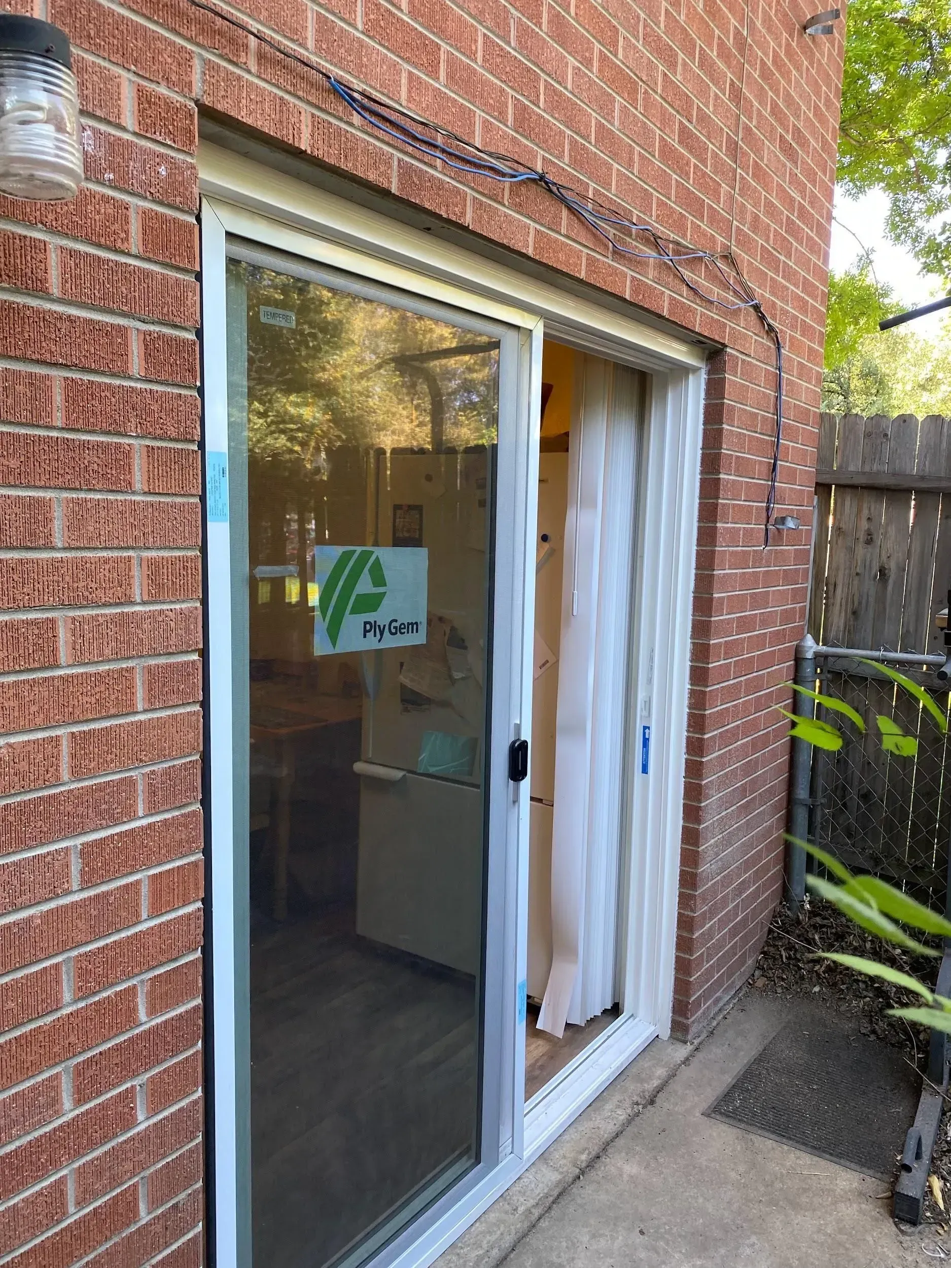 Sliding glass door in brick building. One side open, curtain inside. Concrete patio outside.