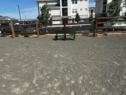 Dog park with gravel ground, wooden fence, and a bench.