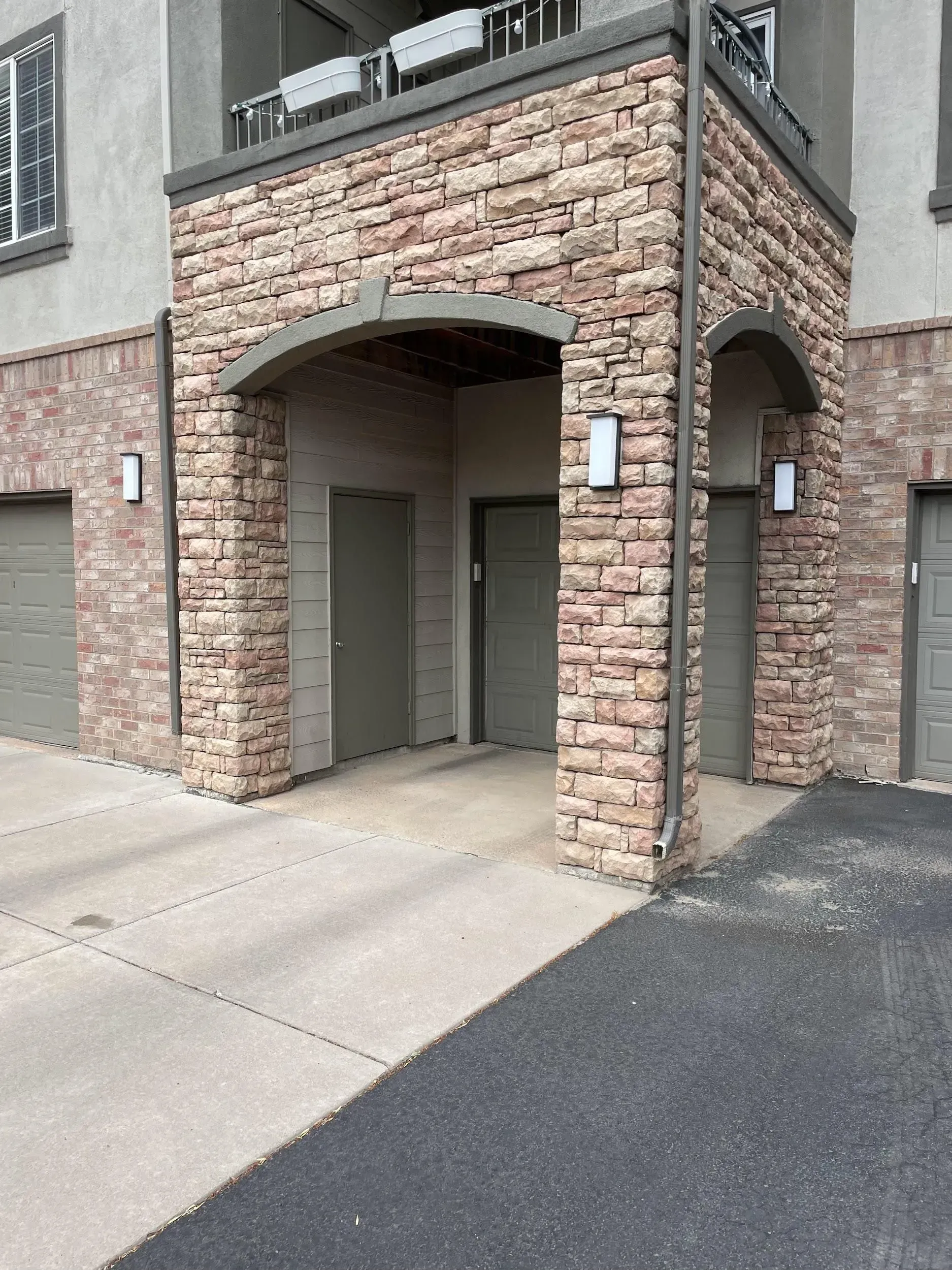 Exterior view of an apartment entrance with brick and stone facade, doors, and garage access.