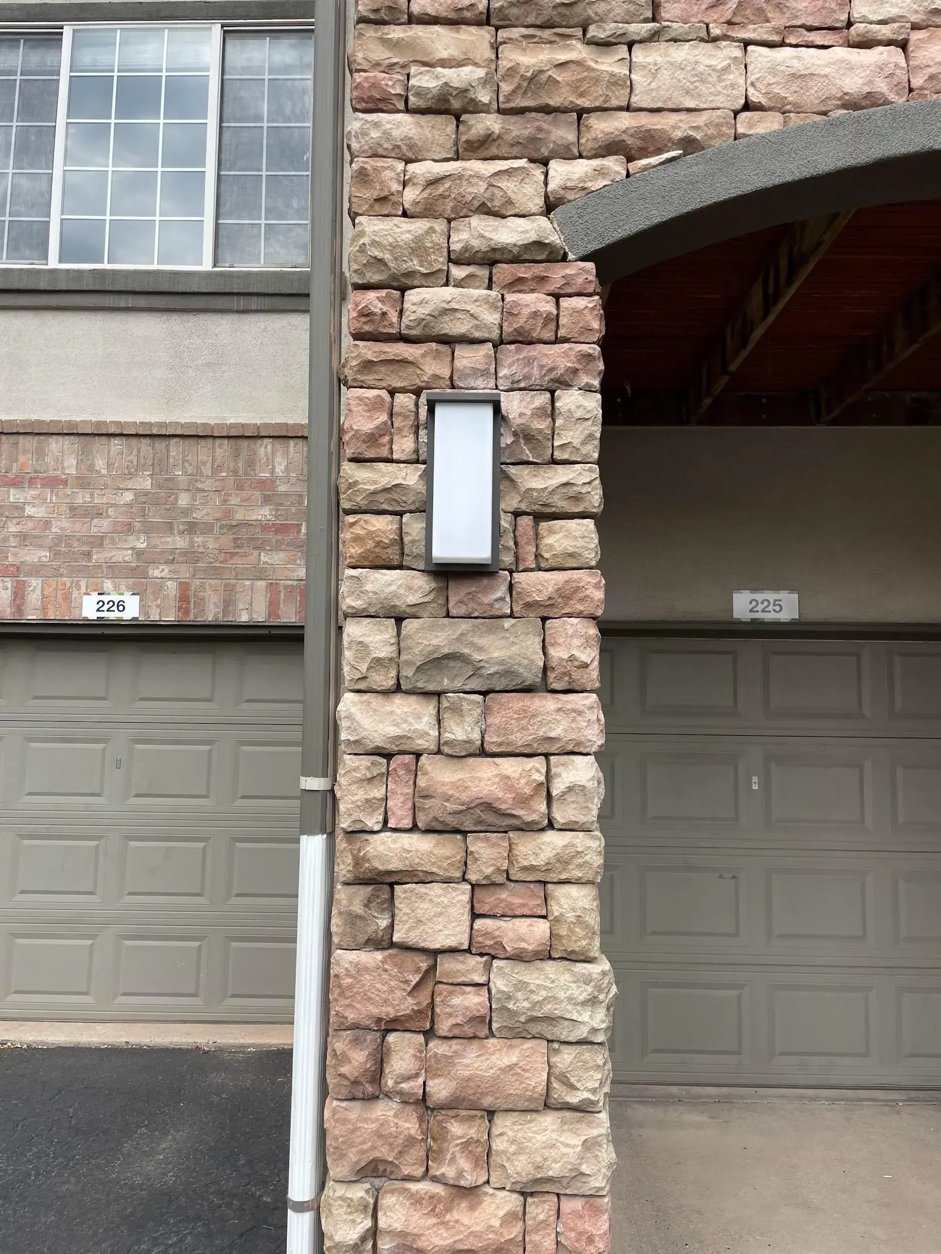 Stone column with rectangular light fixture, between two garage doors.