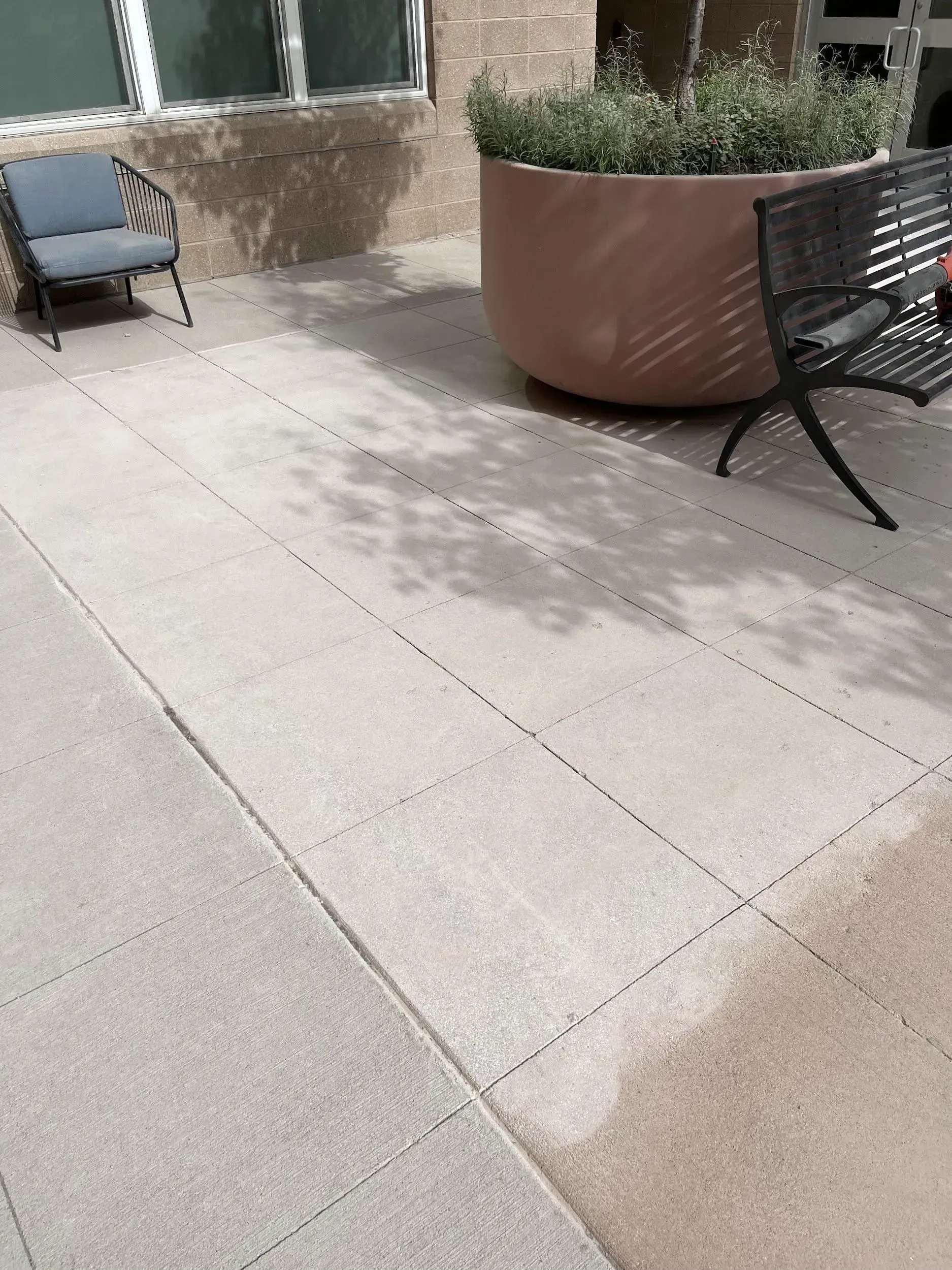Patio with seating, large planter, and textured concrete flooring; dappled sunlight.