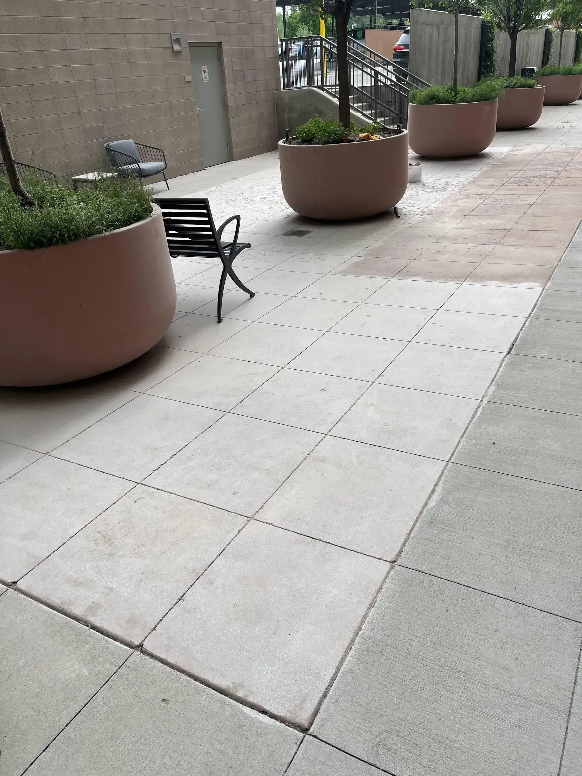 Sidewalk with large planters, a bench, and a building in the background.