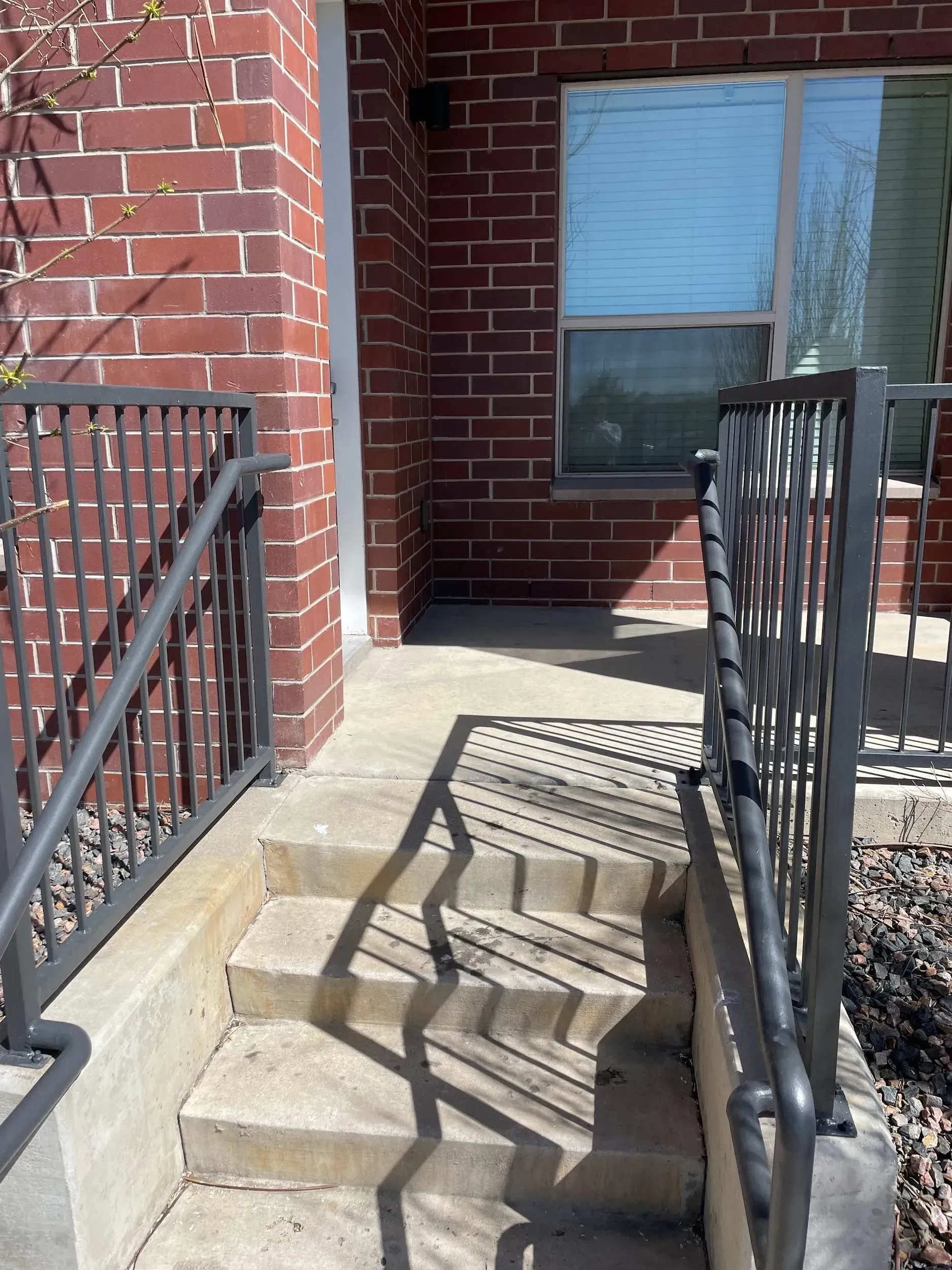 Brick building entrance with concrete steps, black railing, and a window.