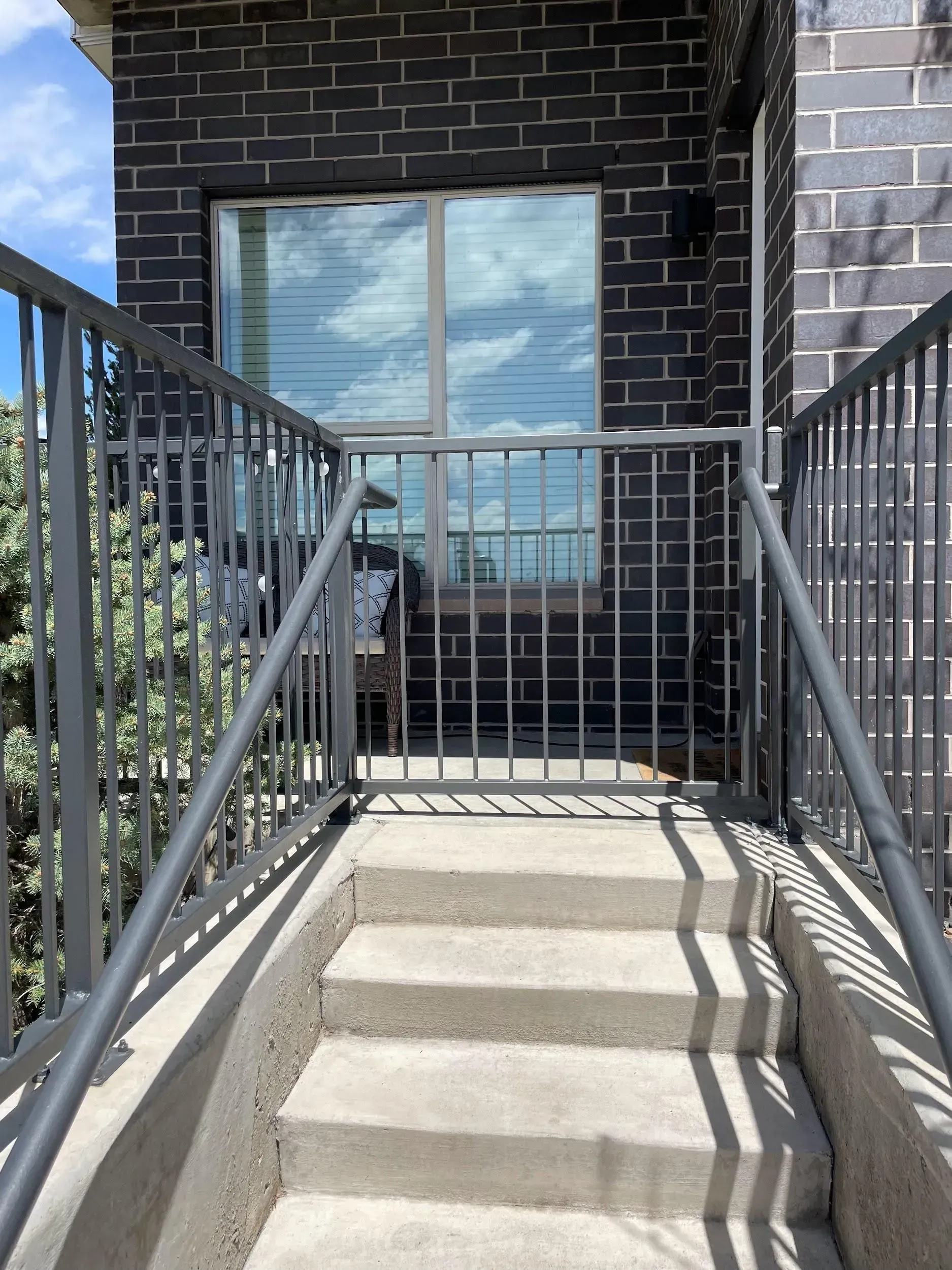 Concrete steps leading up to a doorway with a metal gate and handrails, against a brick wall.