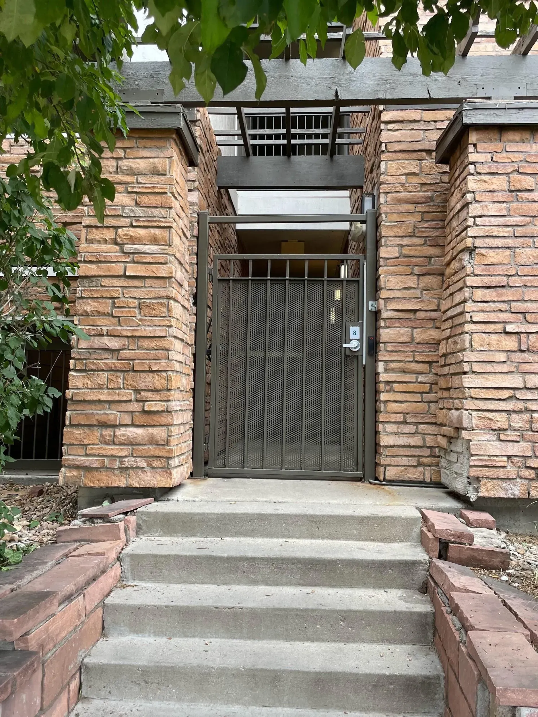 Stone entrance with metal gate, steps. Brown brick pillars.