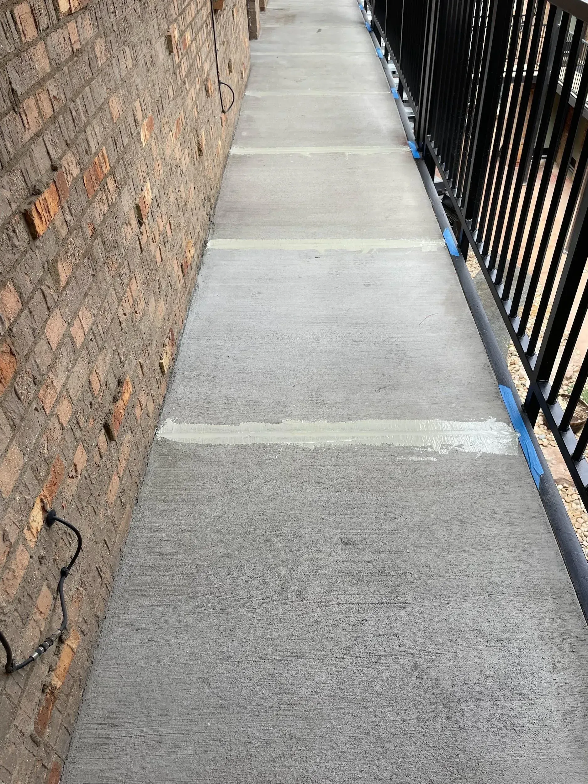 Concrete walkway next to a brick wall and black railing.