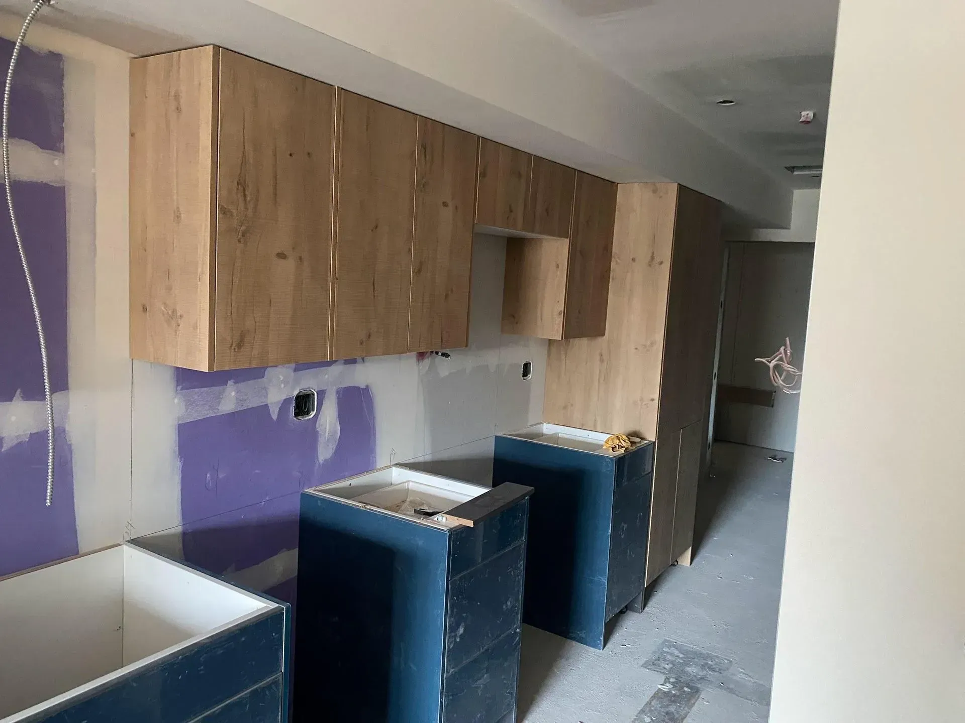 Kitchen under construction with light wood cabinets, dark blue base cabinets, and unfinished walls.