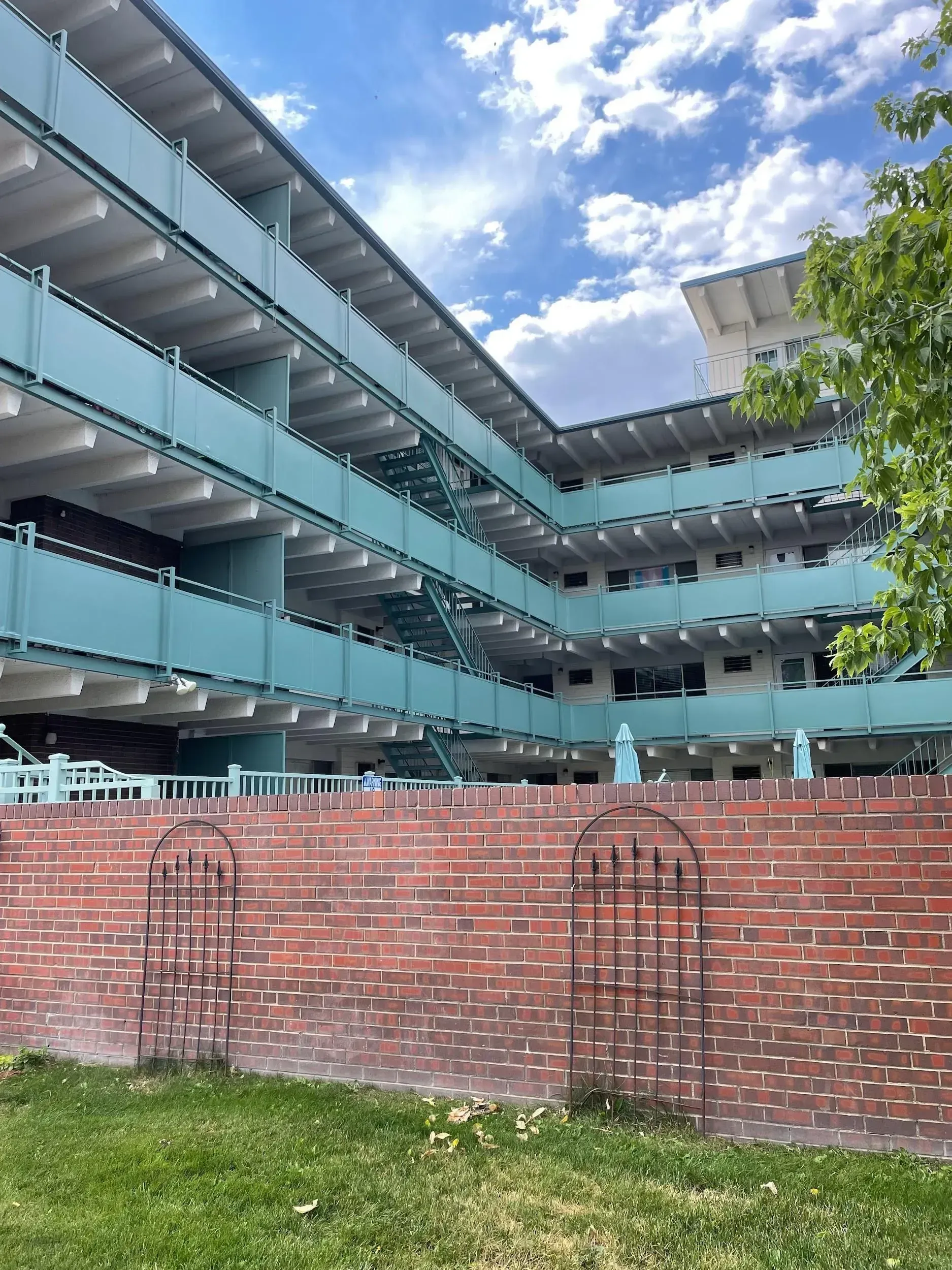 Brick wall in front of a multi-story, turquoise-colored building under a cloudy sky.