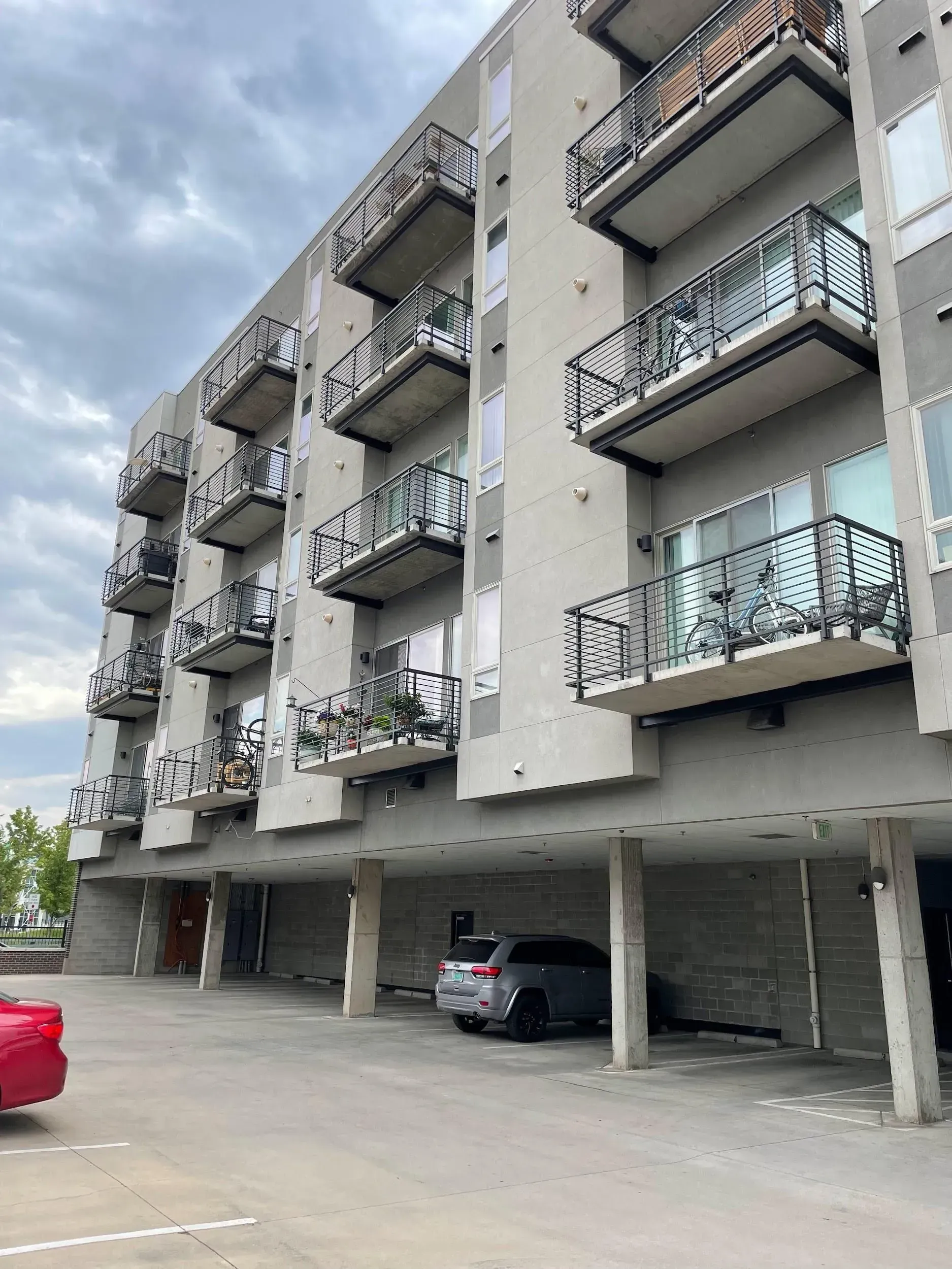 Multi-story apartment building with balconies and parking underneath on a cloudy day.